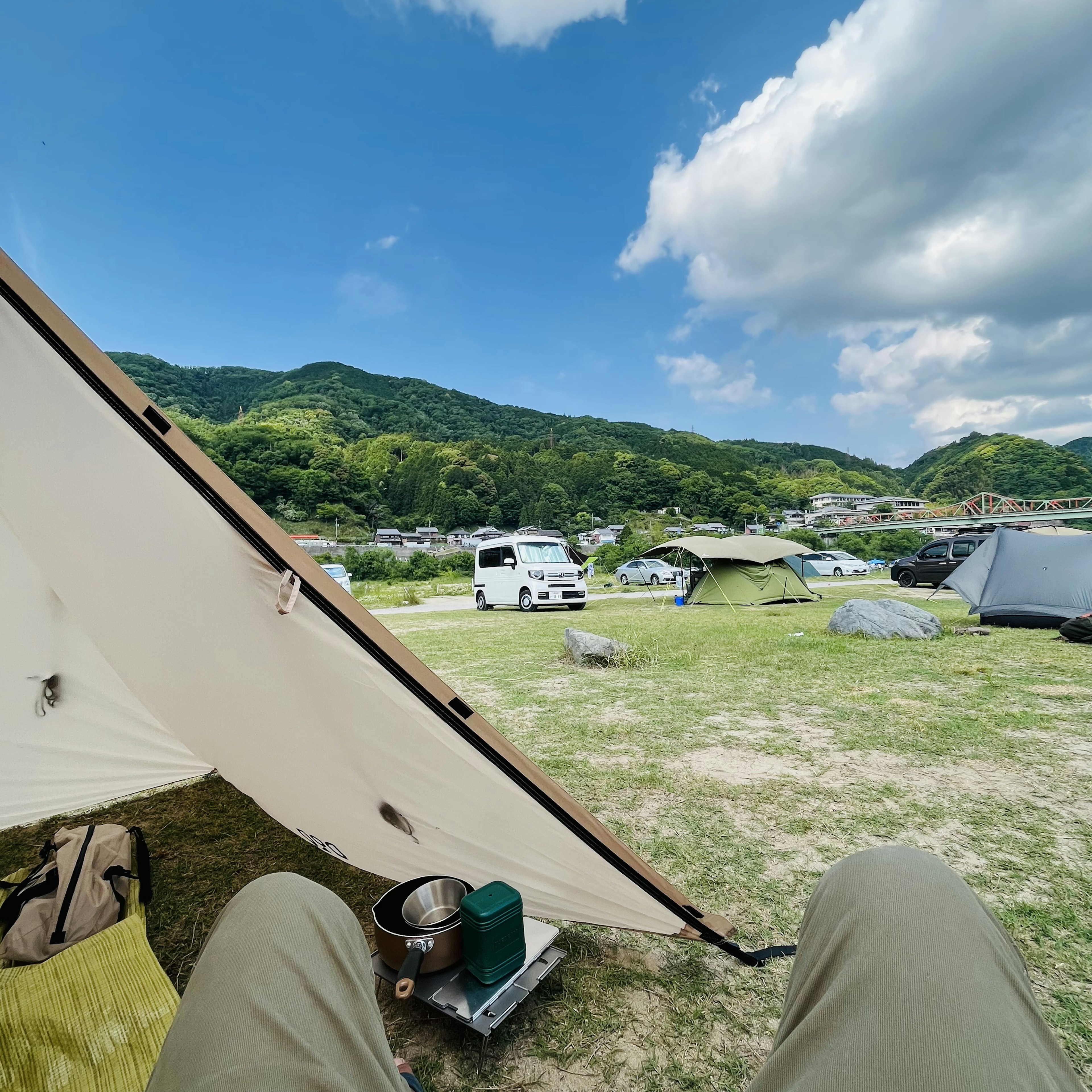 キャンプ場の風景、青い空と緑の山々、テントと車が見える