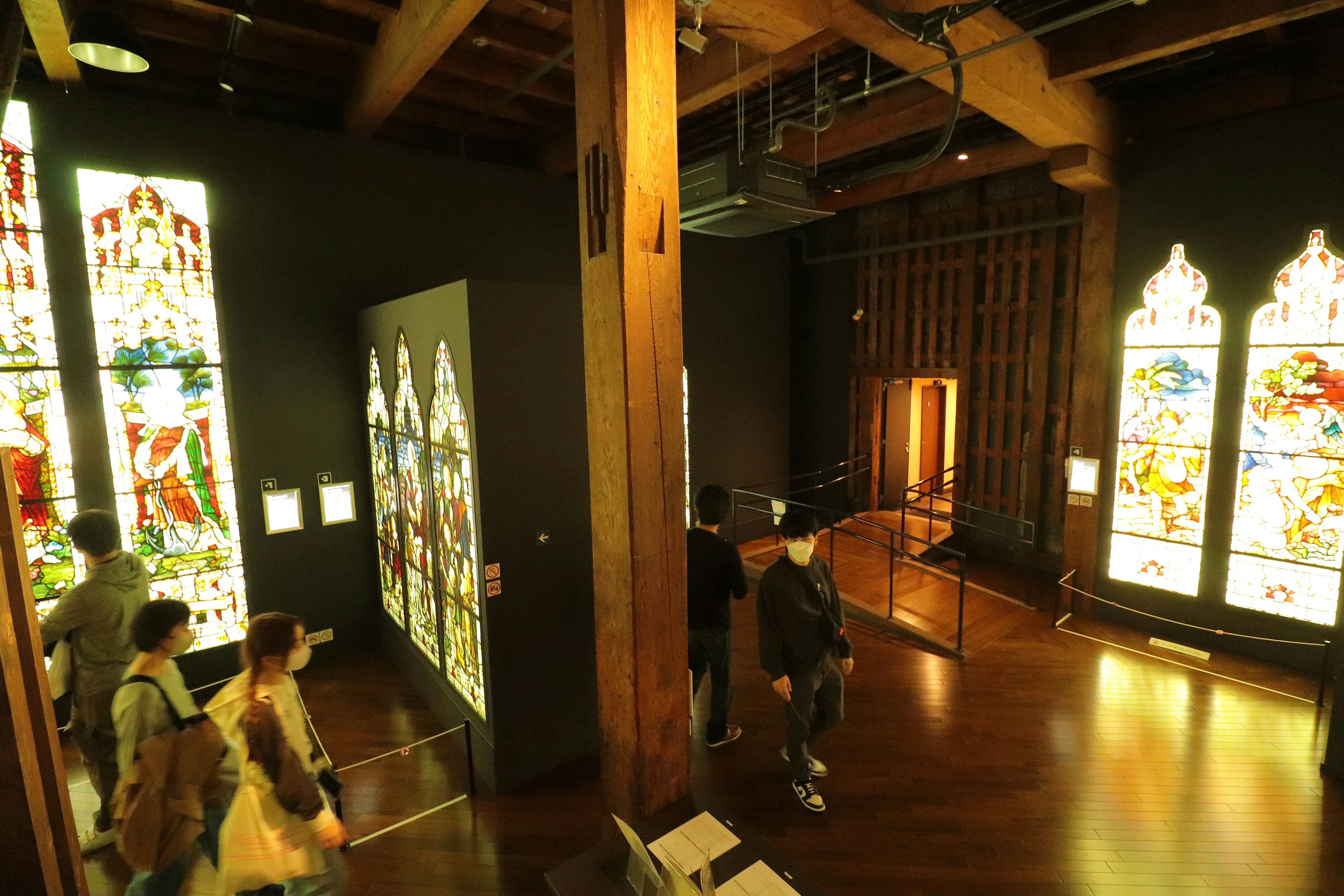 Interior de un museo con vigas de madera y ventanas de vidrio de colores