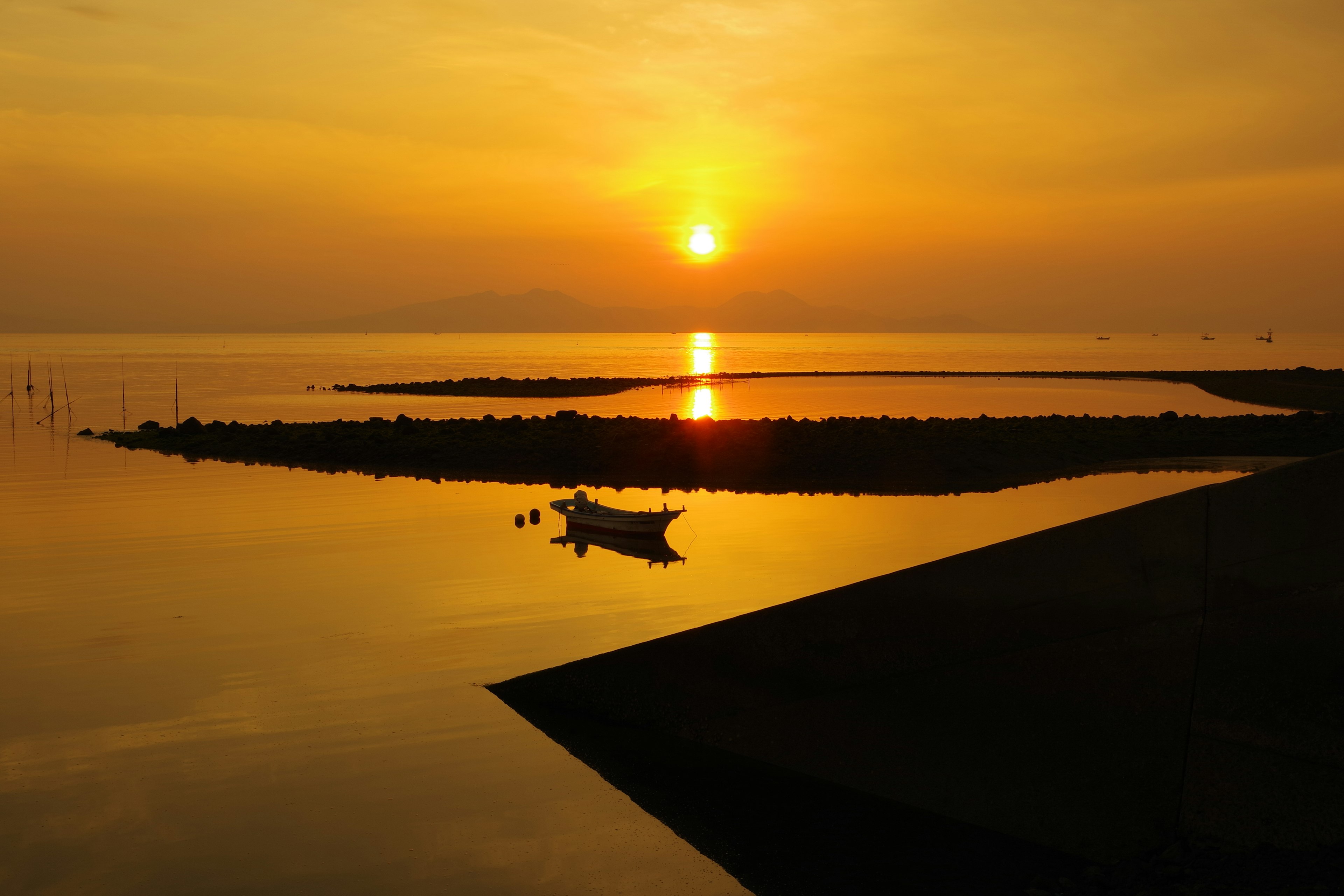 Ruhige Seelandschaft mit Sonnenuntergang, der sich im Wasser spiegelt kleines Boot, das nahe am Ufer schwimmt