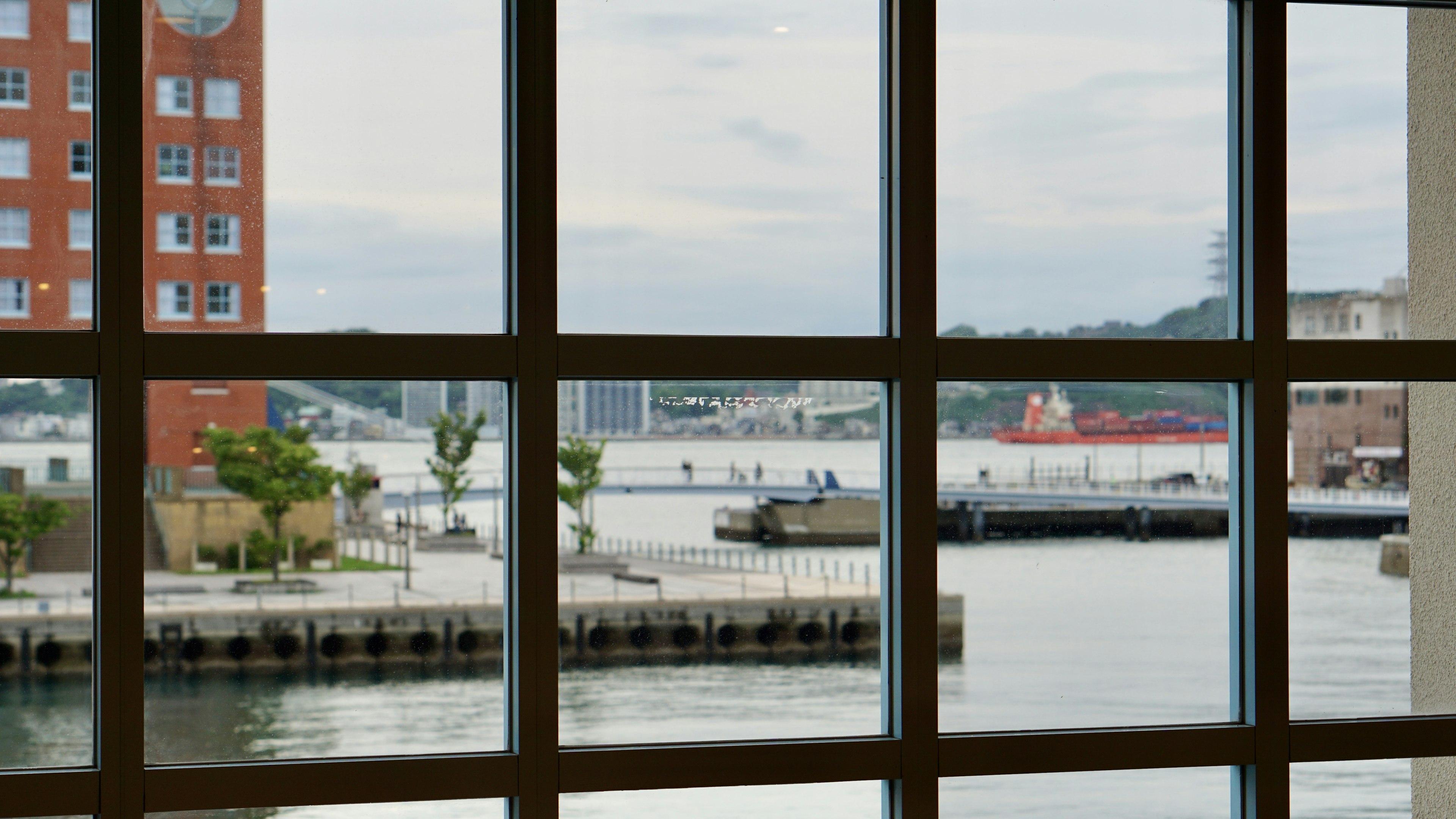 Vista di un porto attraverso una finestra con barche e acque calme, edifici nelle vicinanze