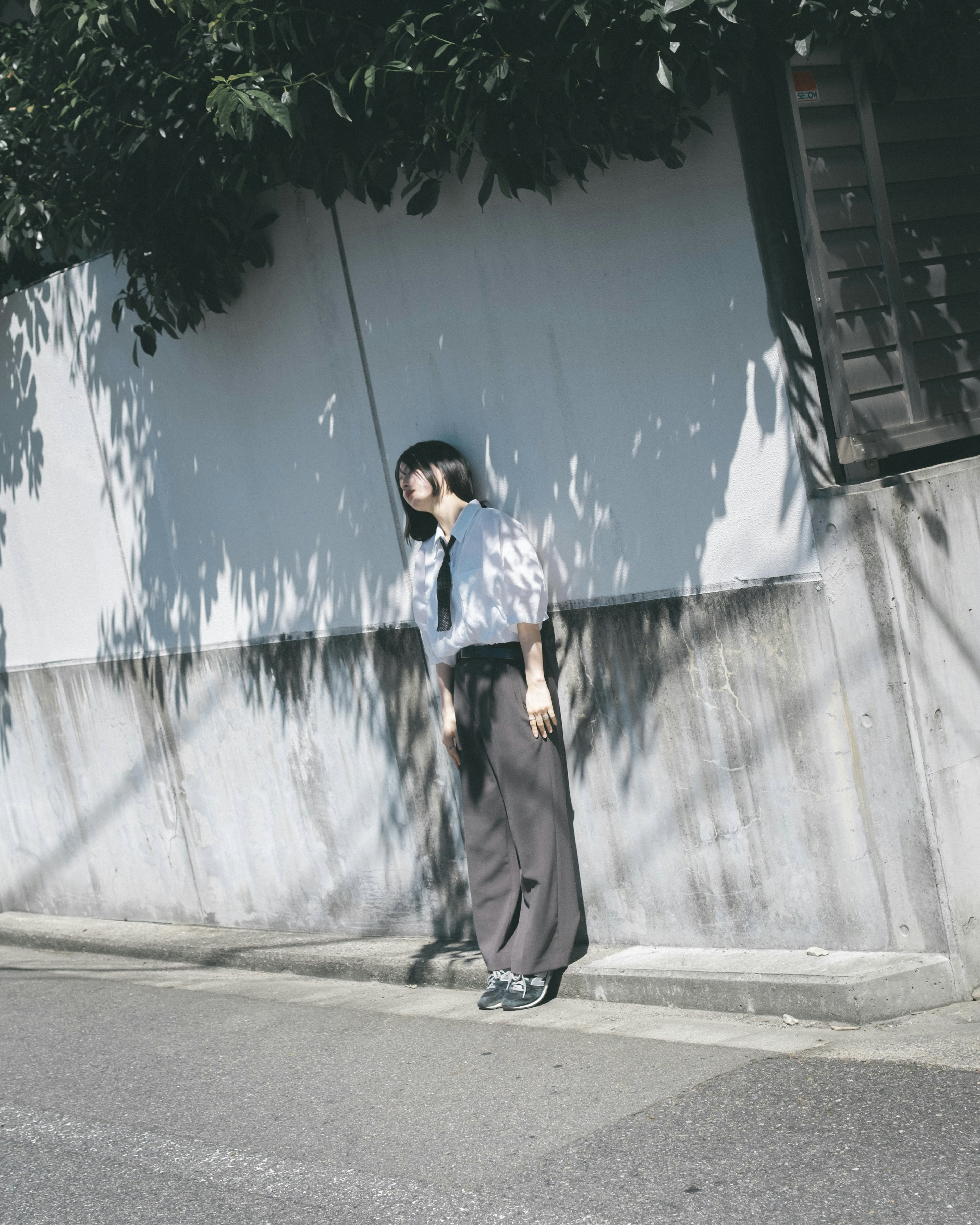 A woman in a white shirt and gray pants standing in front of a wall with shadows