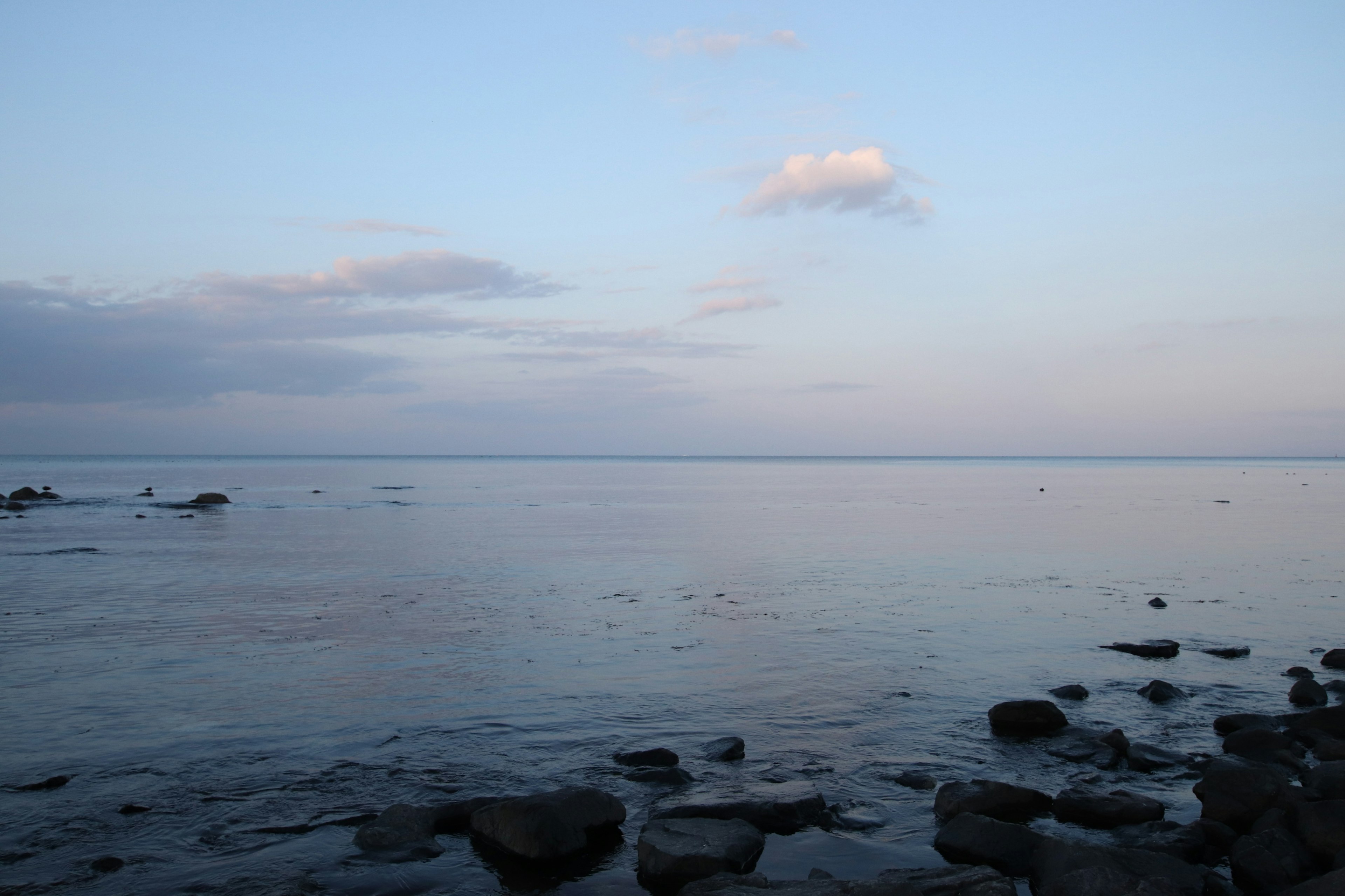 Lanskap laut tenang dengan tepi pantai berbatu dan langit senja yang lembut