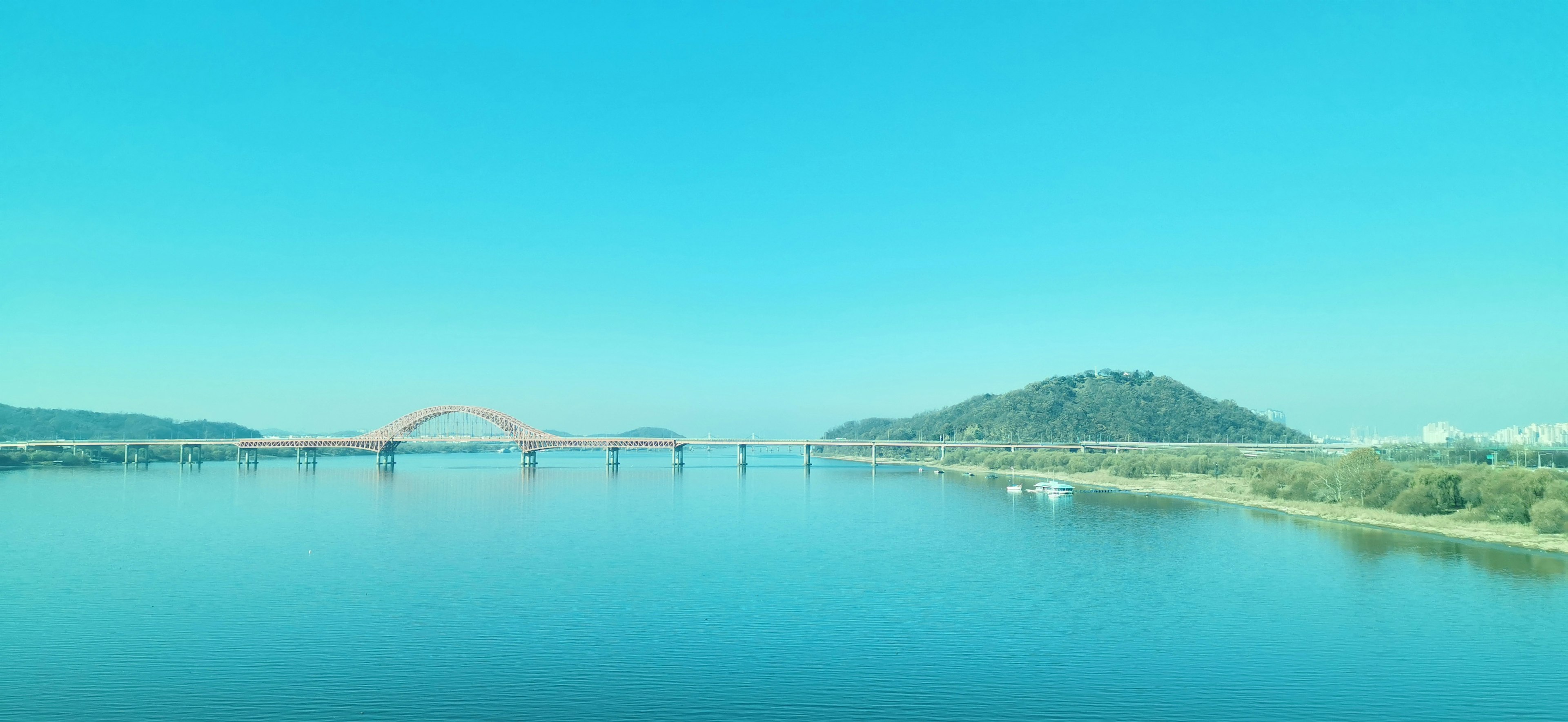 Vista panorámica de un río con cielo azul brillante y un puente y una colina verde visibles