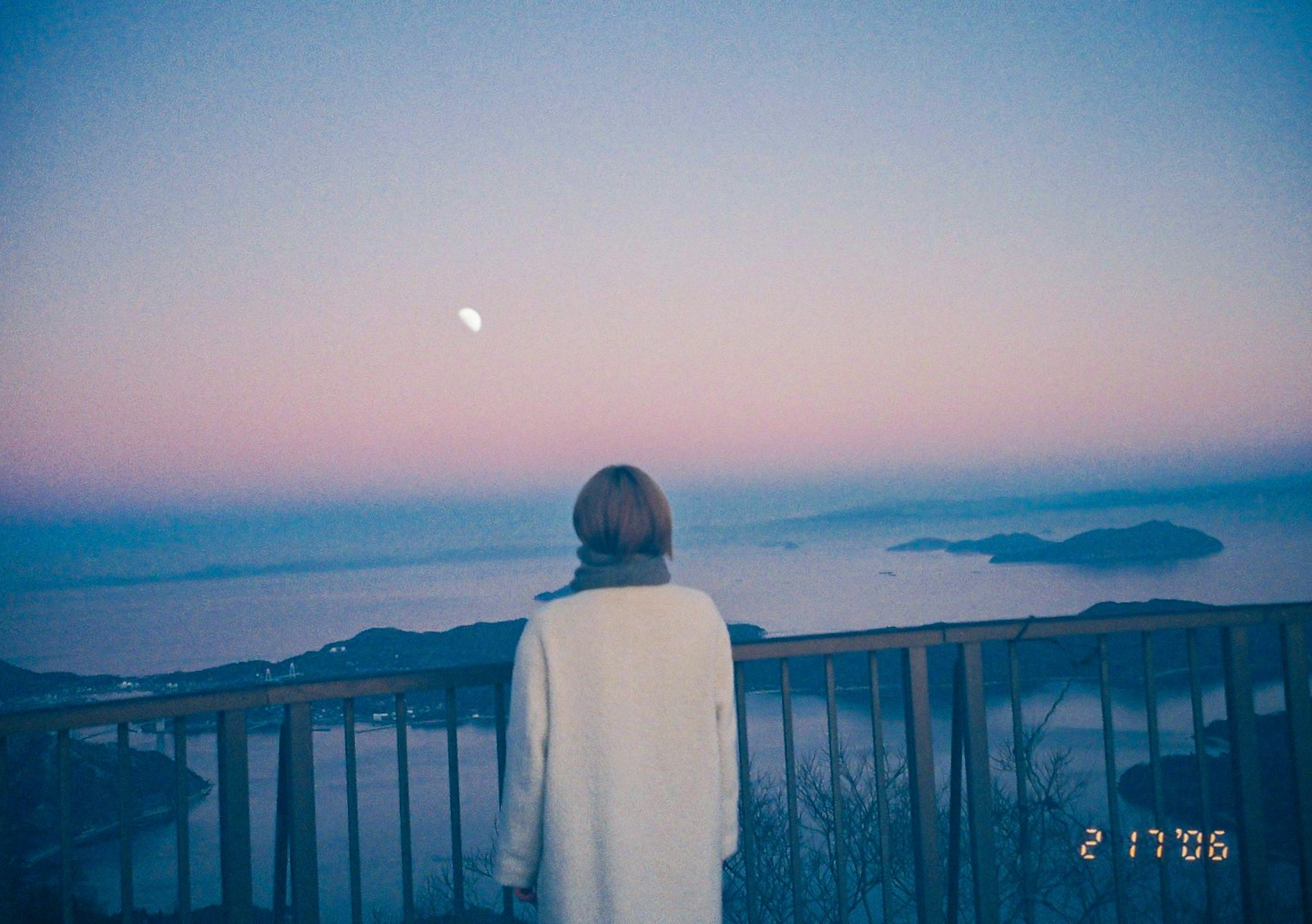 Woman in white coat gazing at the dusk sea with moon in the sky