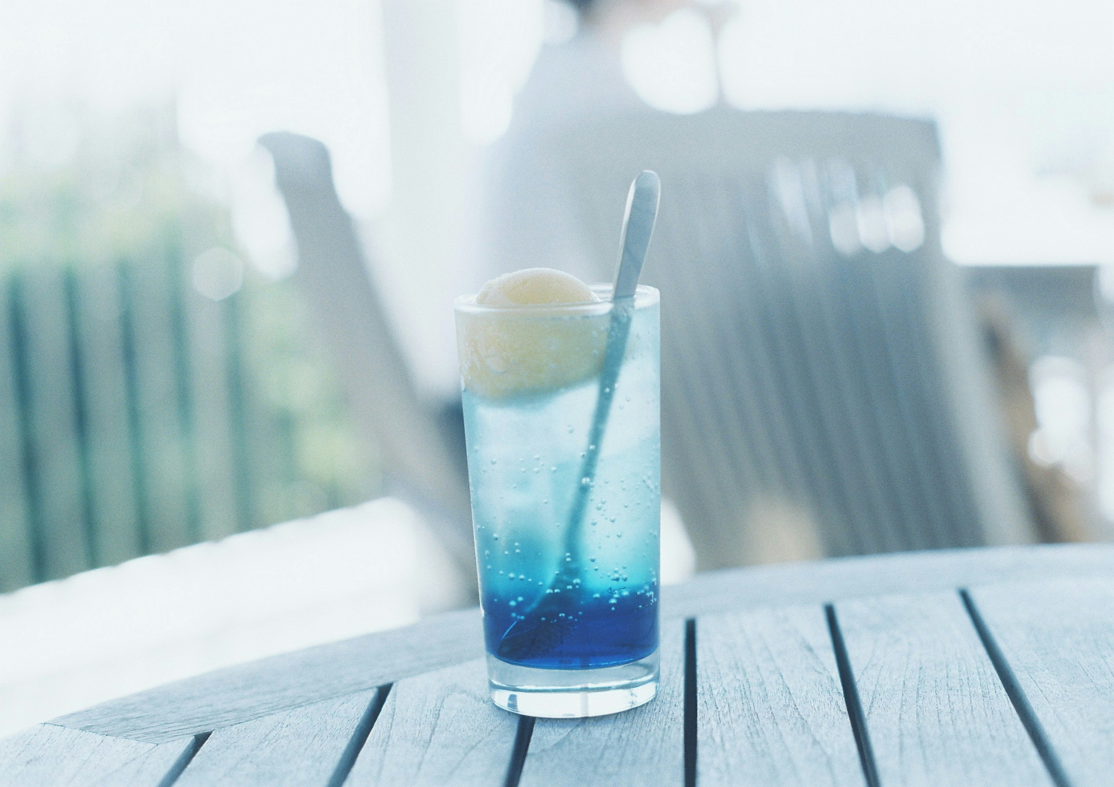 Ein Glas mit blauer Flüssigkeit und einer Kugel Eis auf einem Holztisch