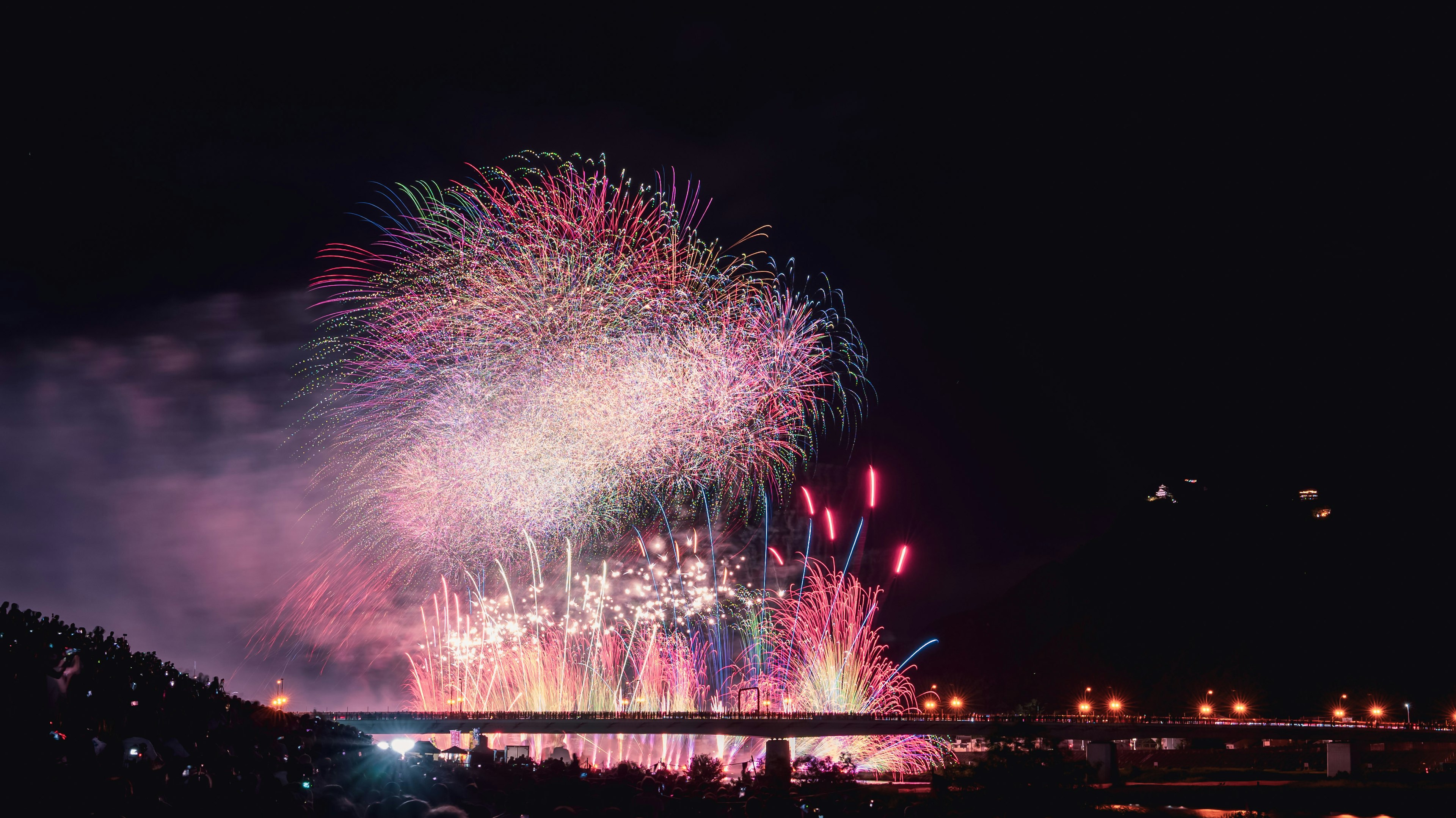 夜空に広がるカラフルな花火のショー 橋の上に灯りが映える