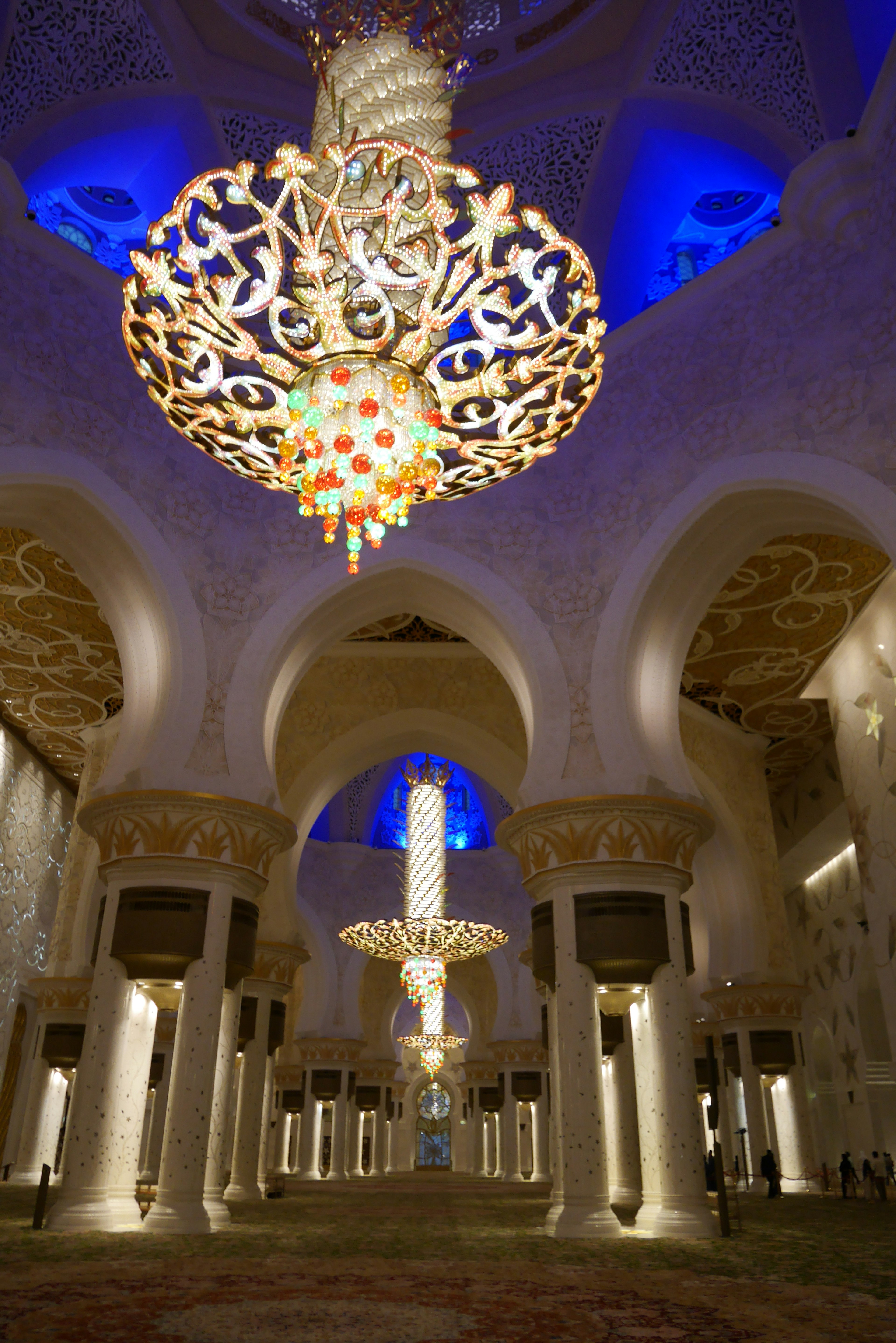 Intérieur d'une grande mosquée avec des lustres ornés et un éclairage bleu