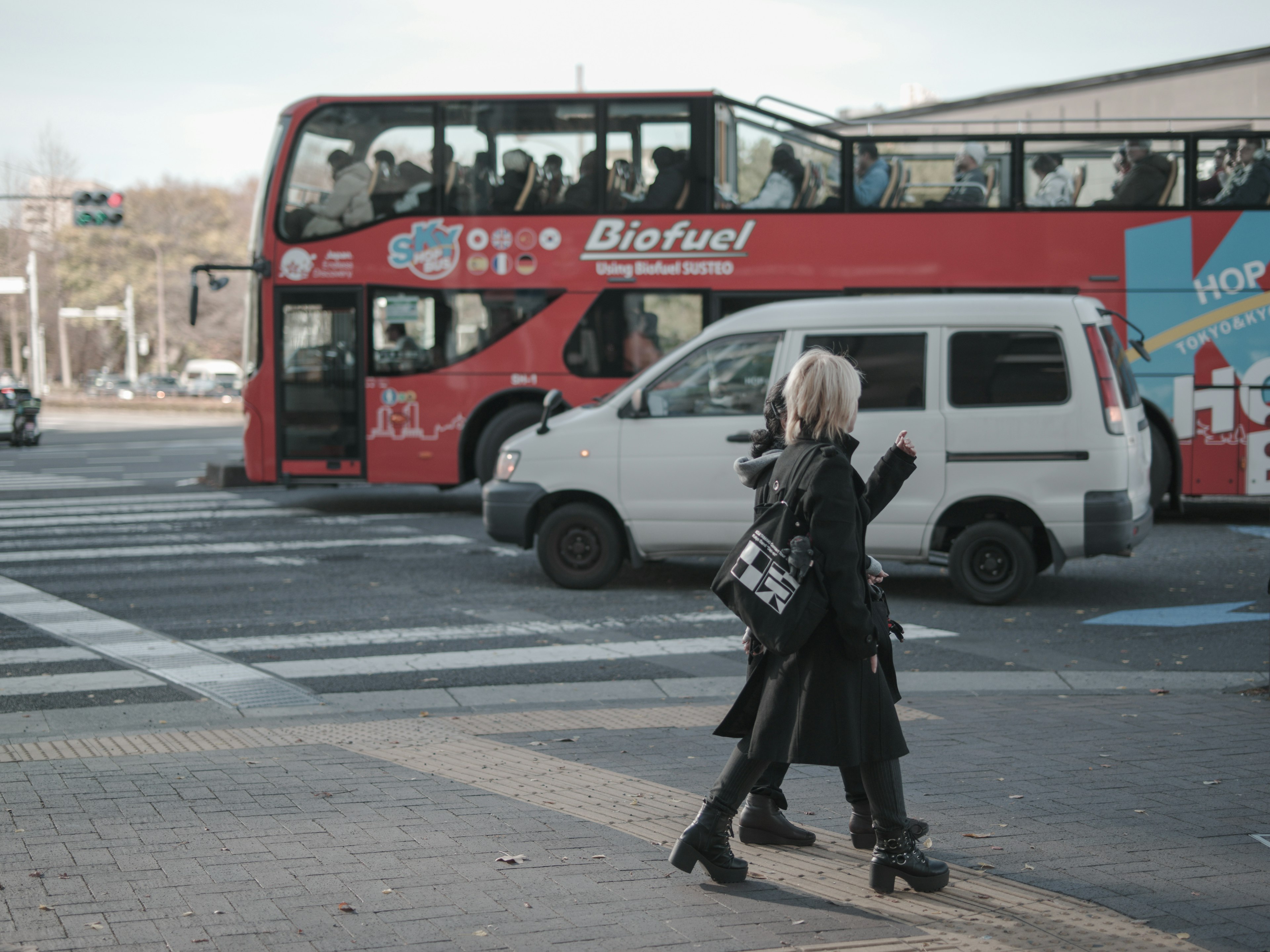 Eine Frau, die an einem Zebrastreifen mit einem roten Bus und einem weißen Fahrzeug im Hintergrund geht