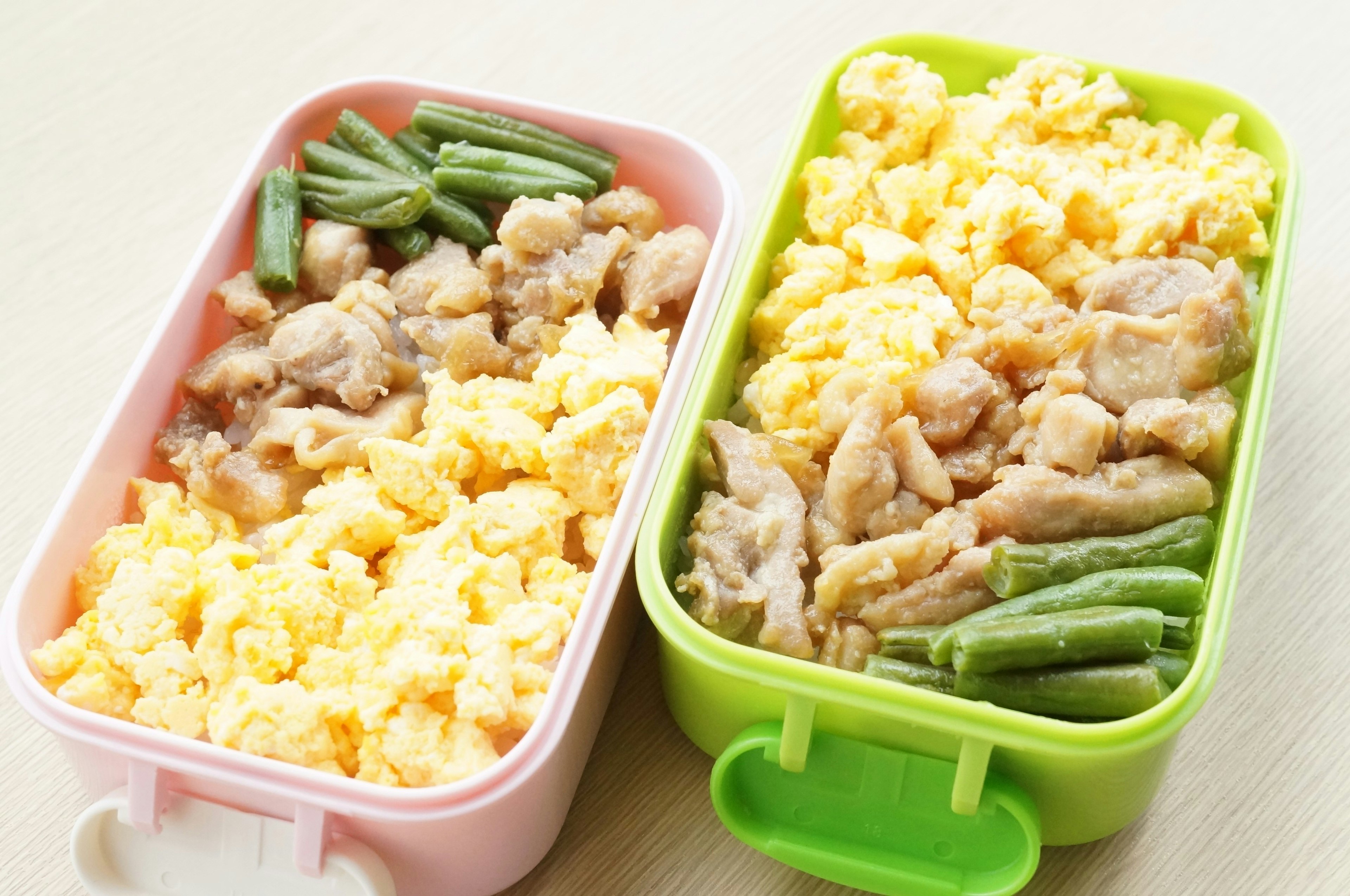 Two bento boxes containing scrambled eggs chicken and green beans