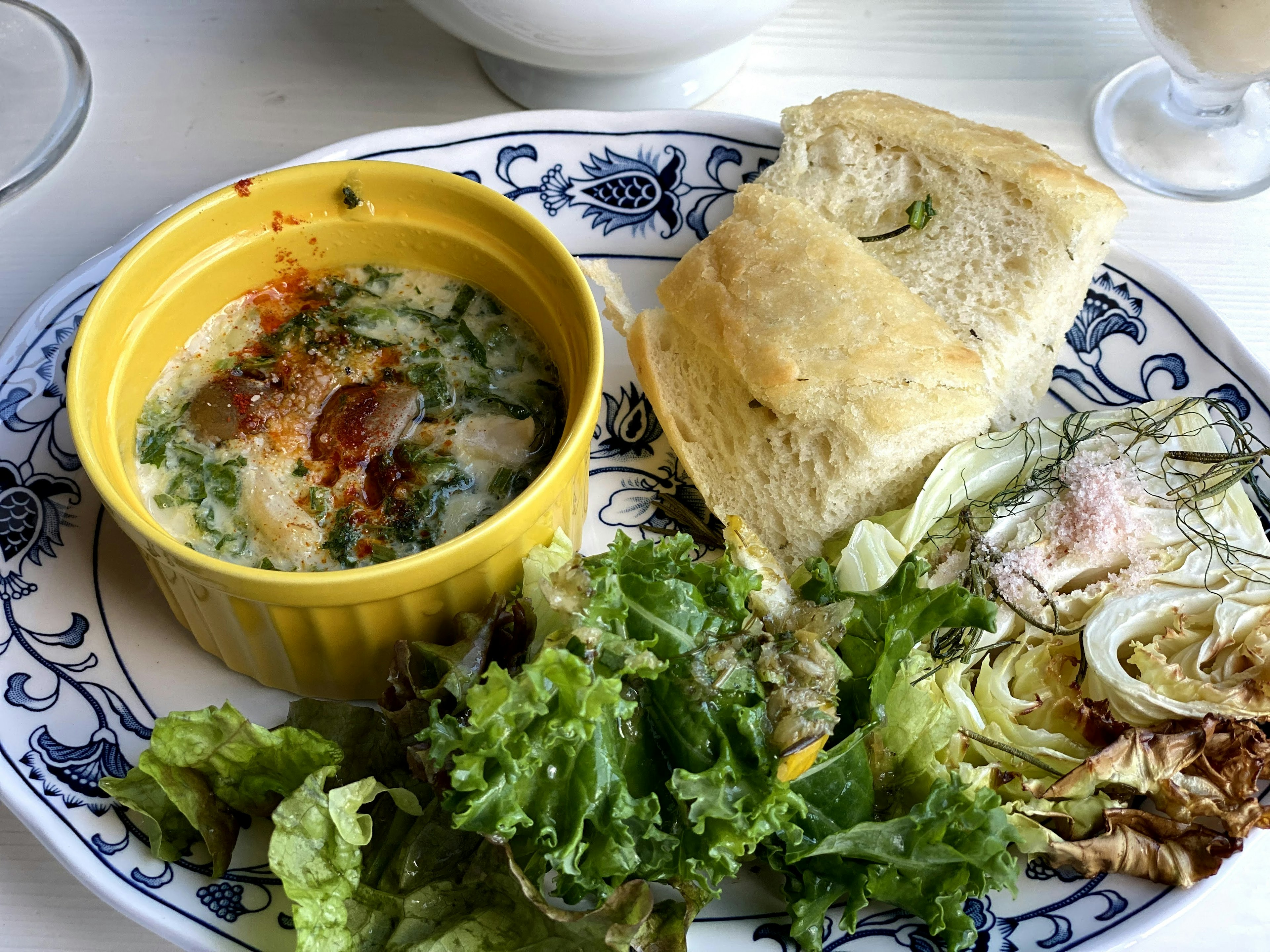 A plate with a yellow bowl of dish salad and bread on the side