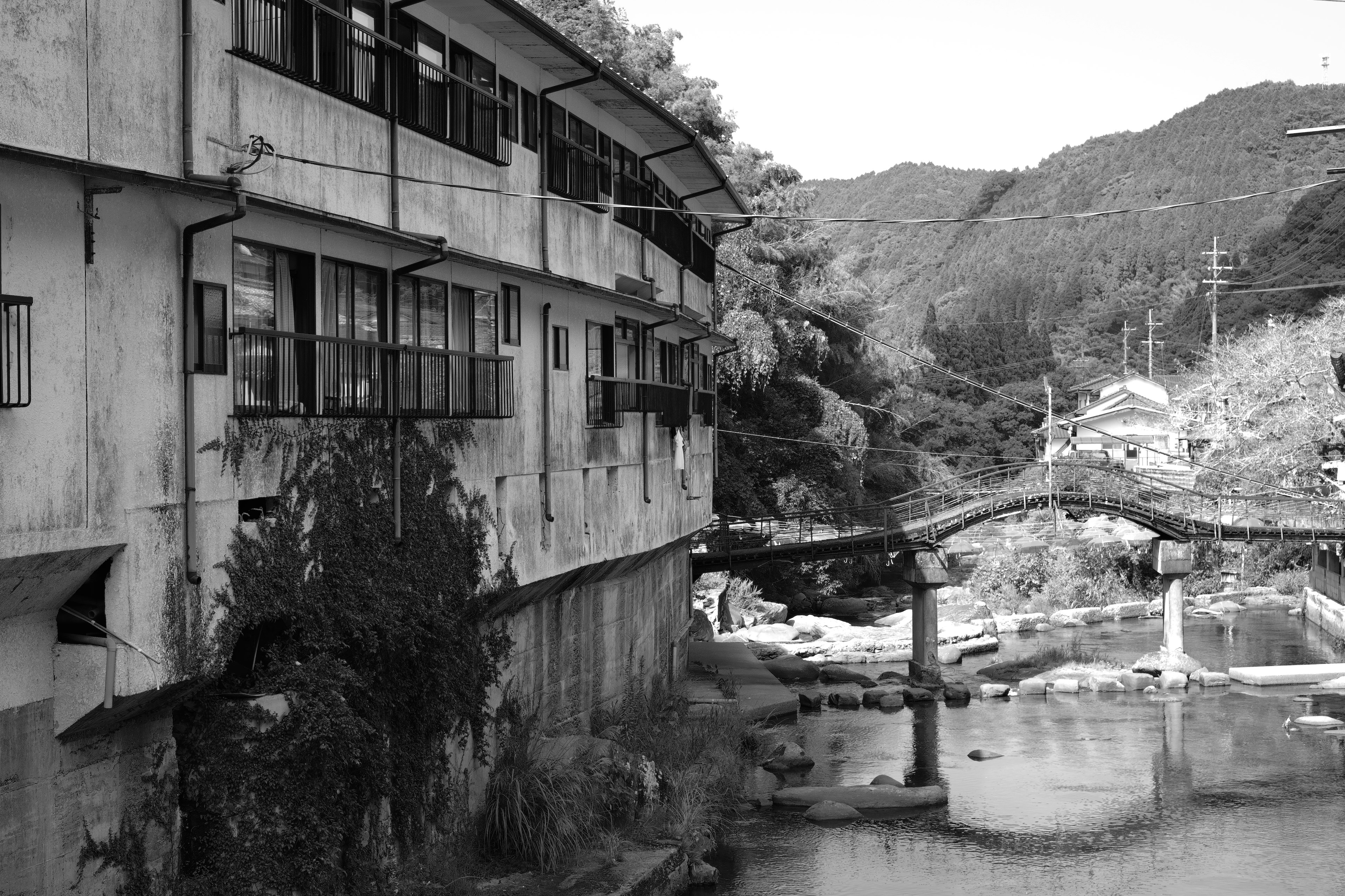 废弃建筑旁的河流，背景有山，黑白照片