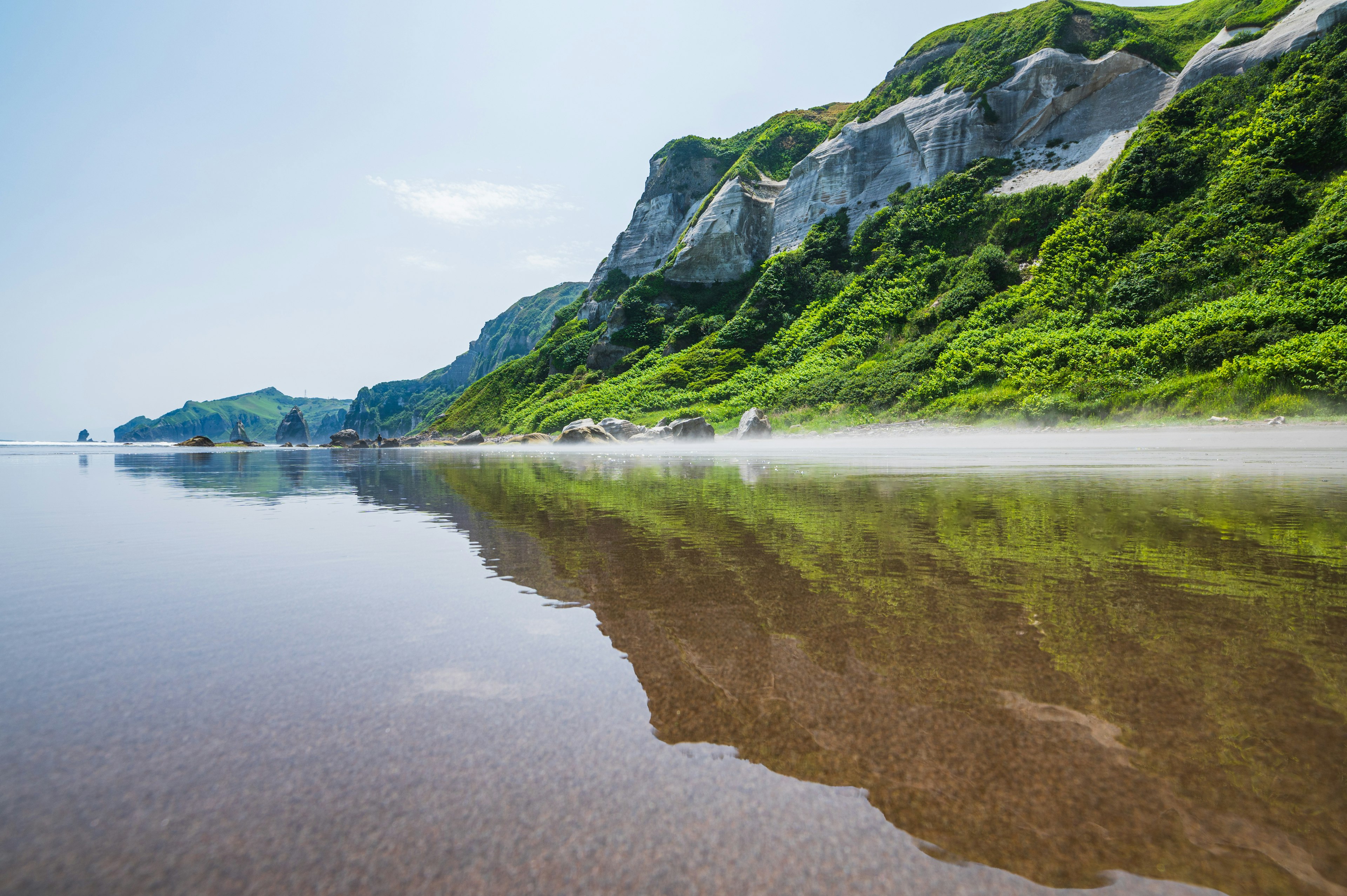 Serene lake reflecting green hills and cliffs under a clear blue sky