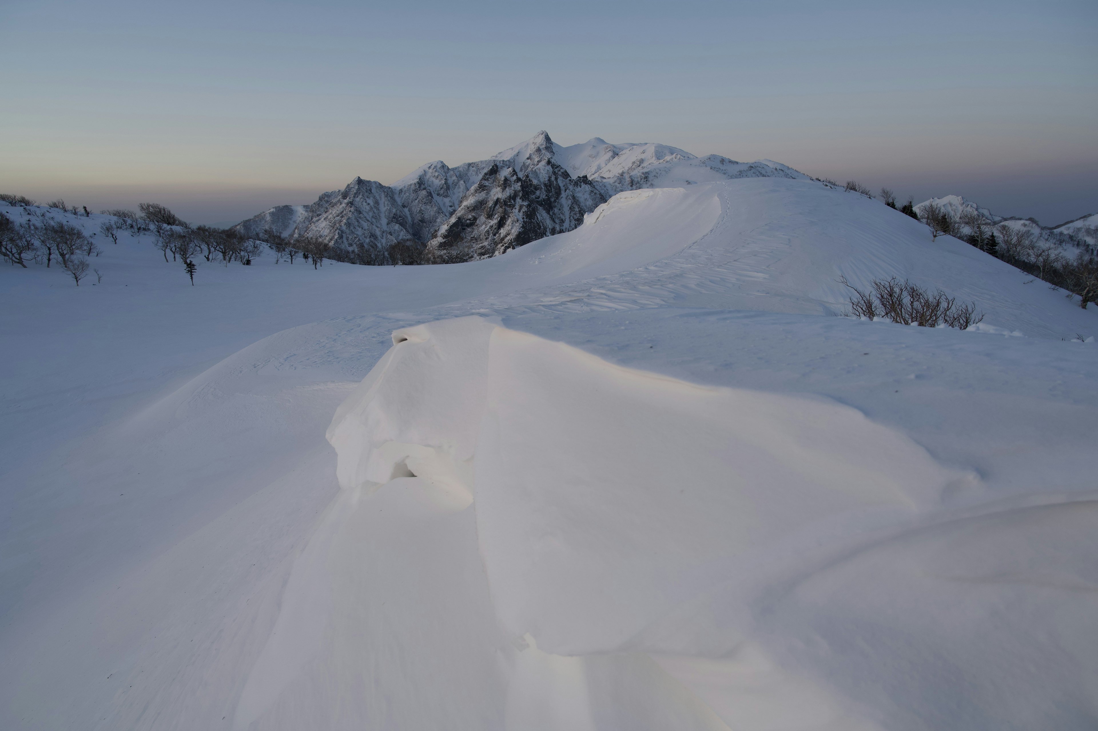 Paesaggio montano innevato con cielo blu chiaro e vette lontane