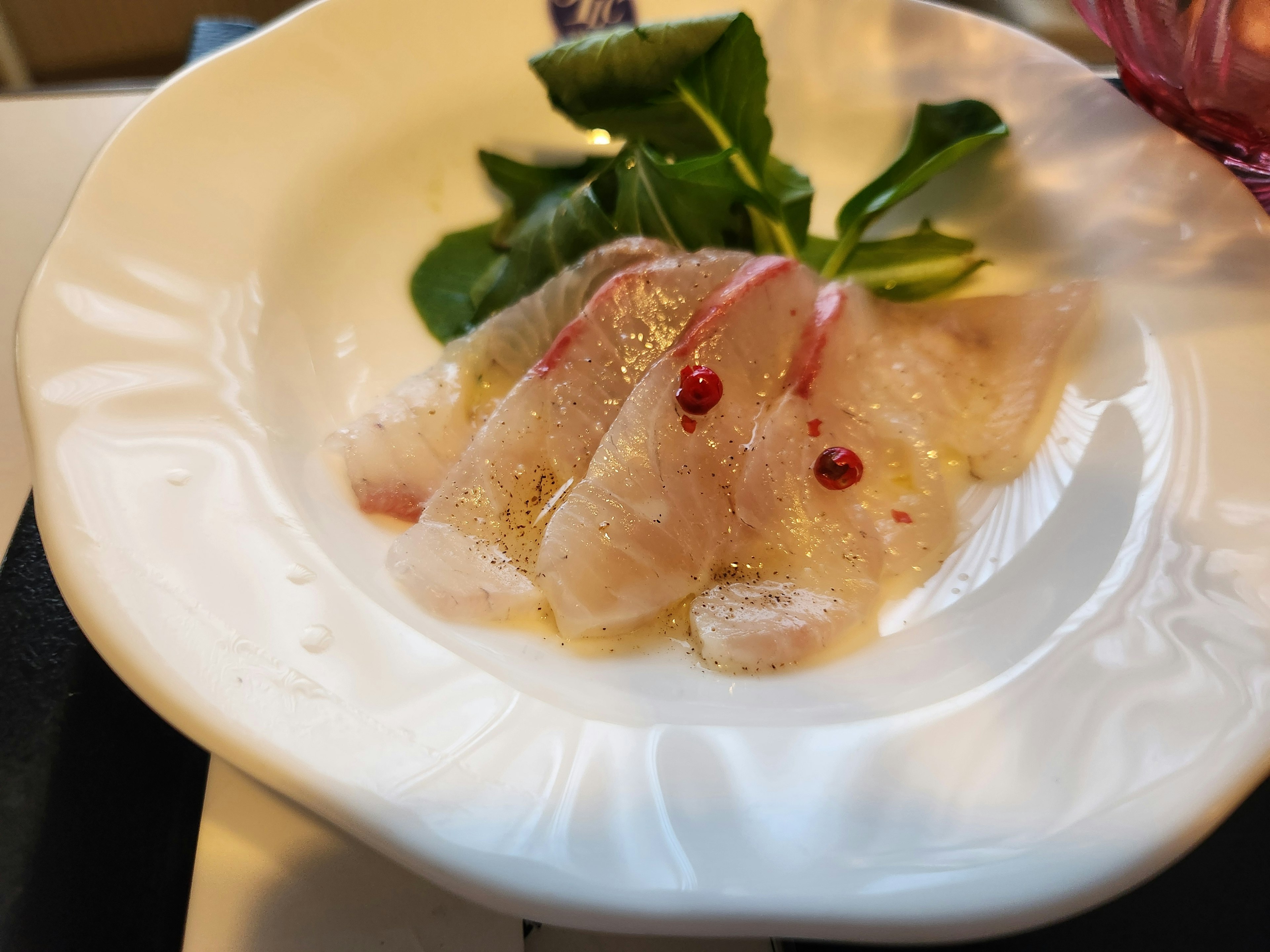 Sliced fish sashimi arranged with herbs on a white plate