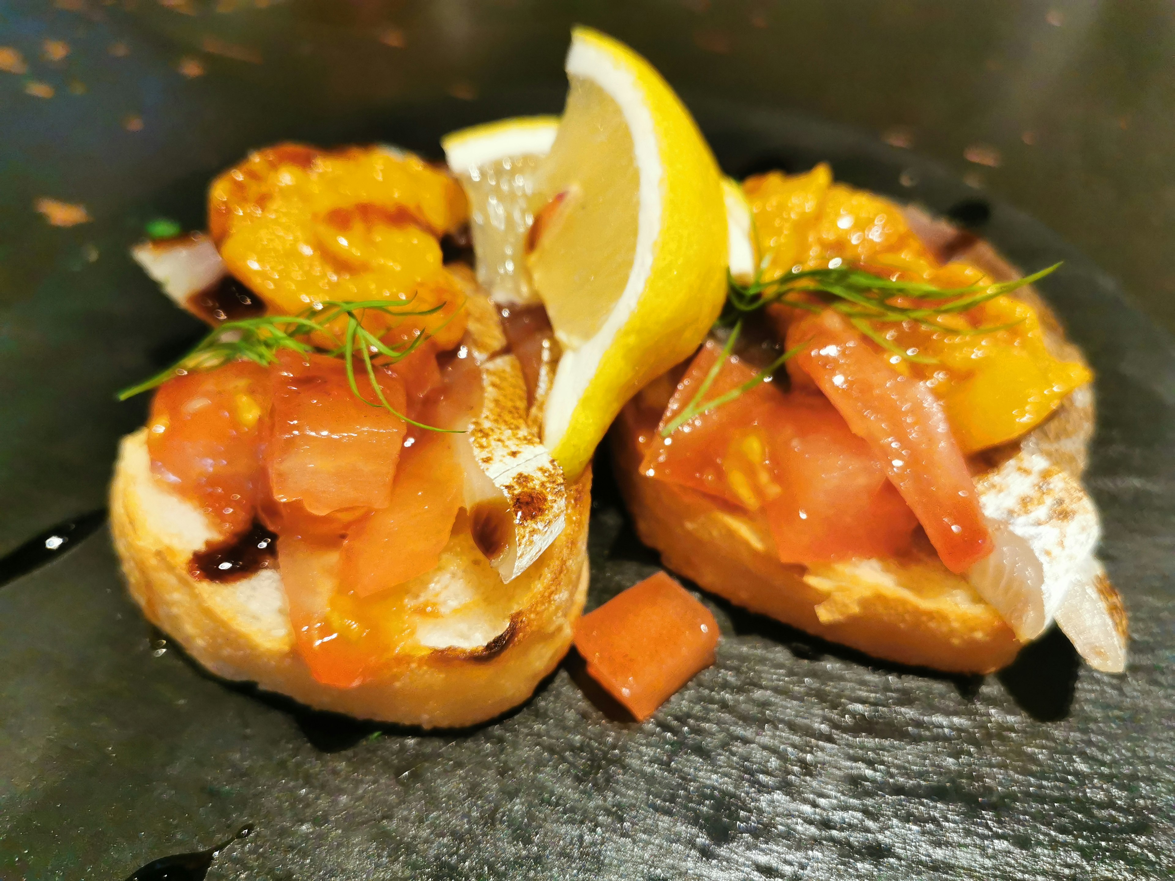 Zwei Scheiben Brot belegt mit frischen Tomaten und orangefarbenen Garnituren serviert mit Zitronenscheiben