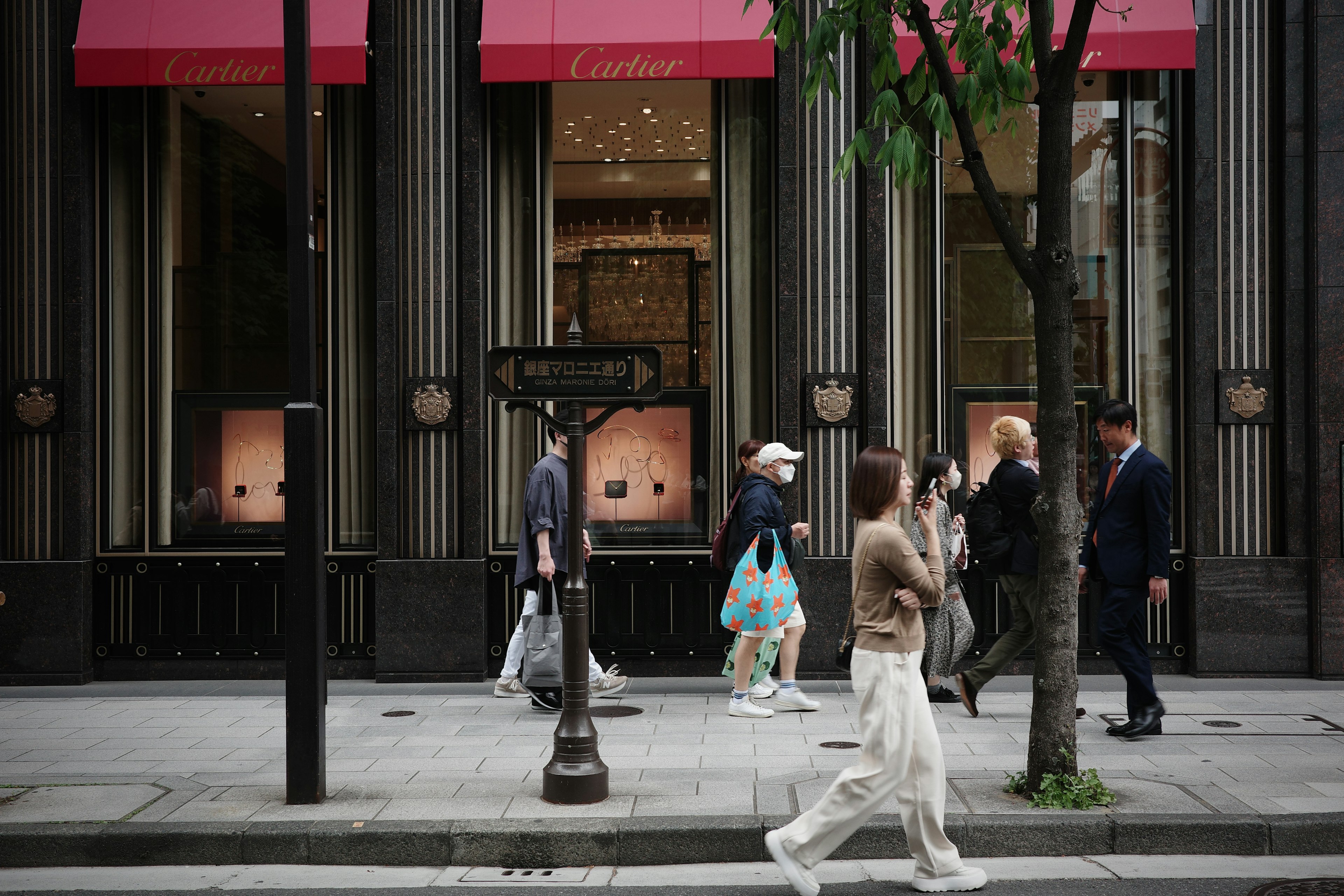 Pedestrians walking by luxury storefronts with pink awnings