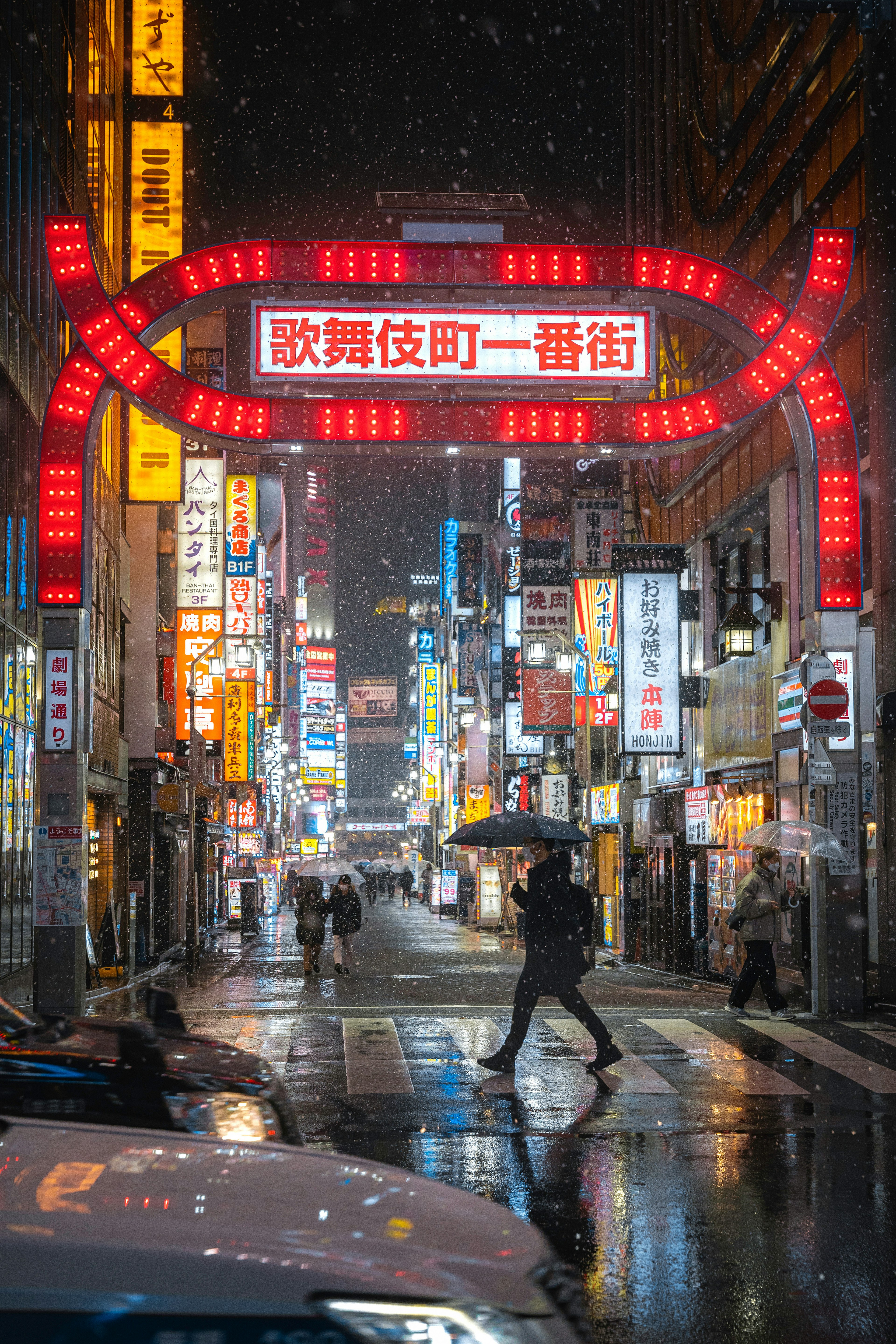 A person with an umbrella walking in a bustling street illuminated by neon signs in the rain