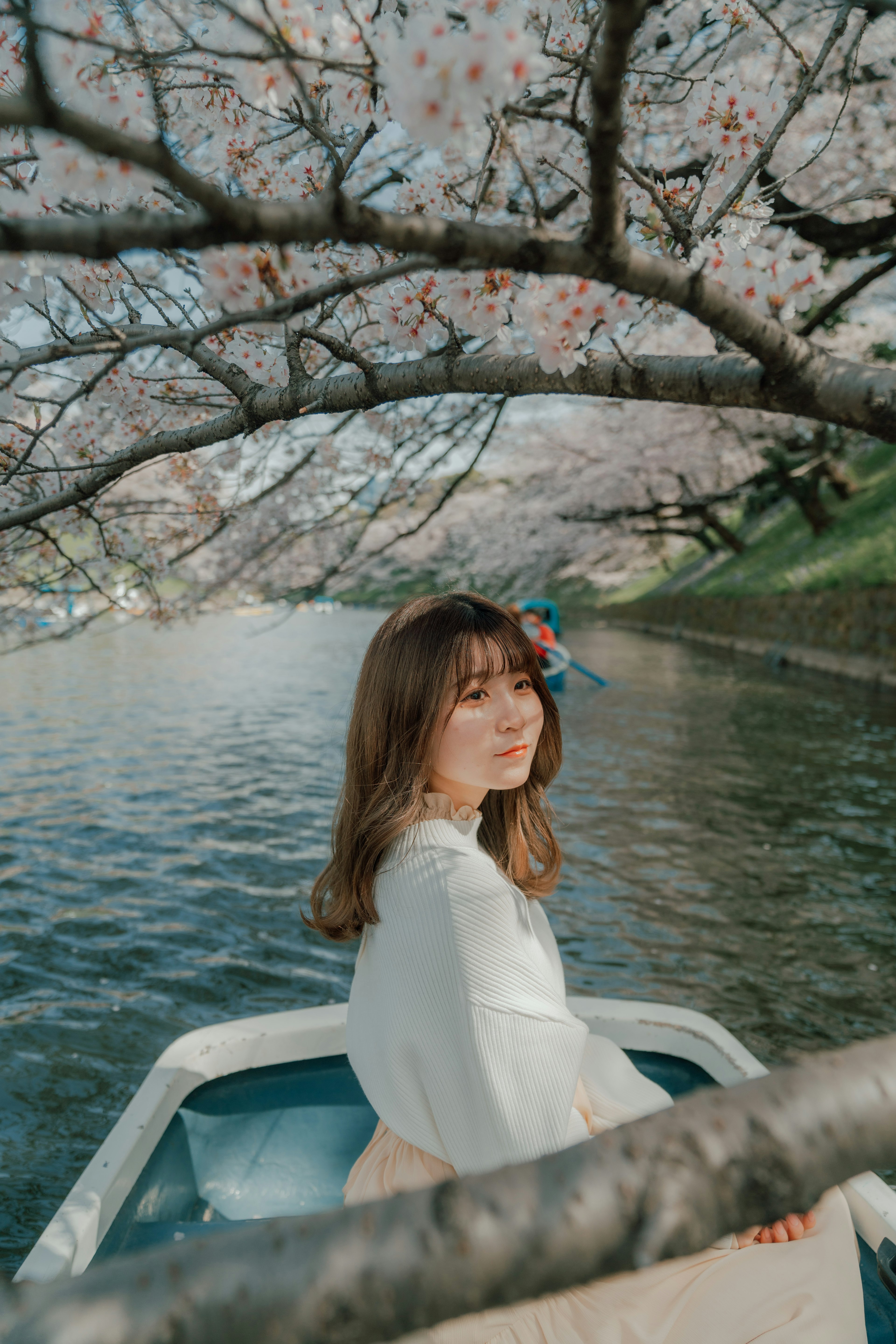 A woman in a boat under cherry blossoms by a tranquil river