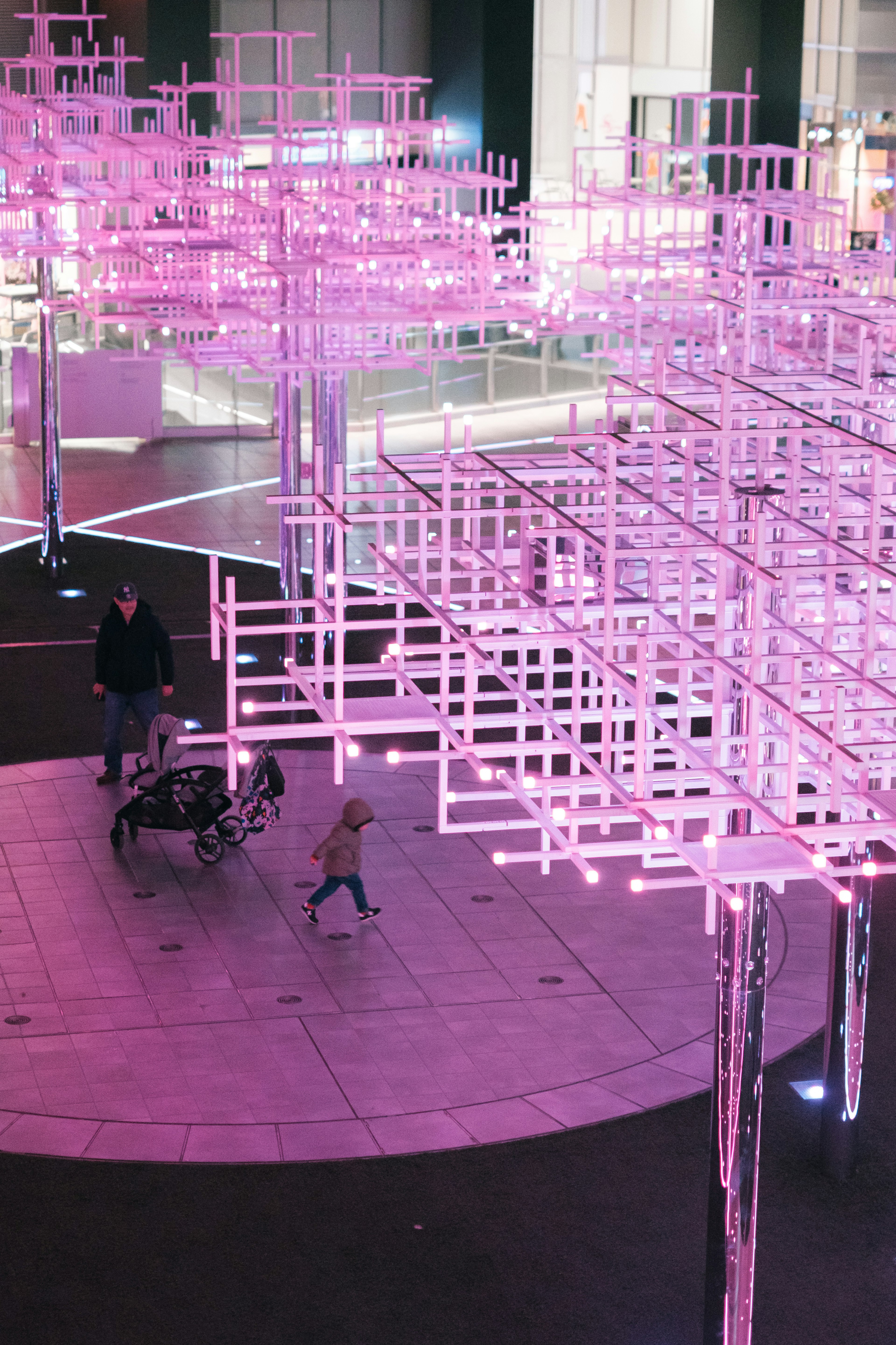 Des personnes marchant sous une installation artistique moderne éclairée en rose