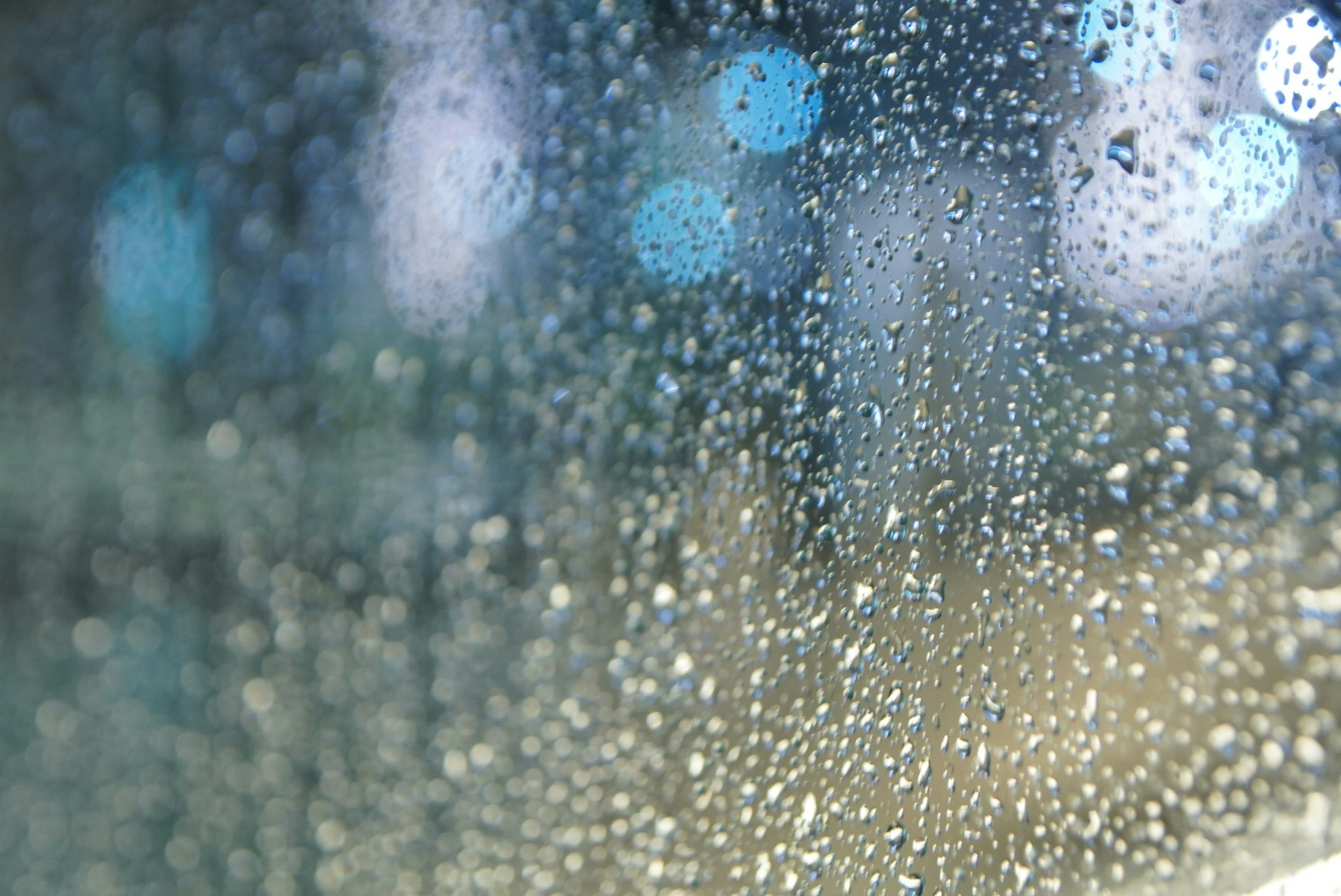 Nahaufnahme eines Fensters mit Wassertropfen und verschwommenen blauen Lichtern im Hintergrund