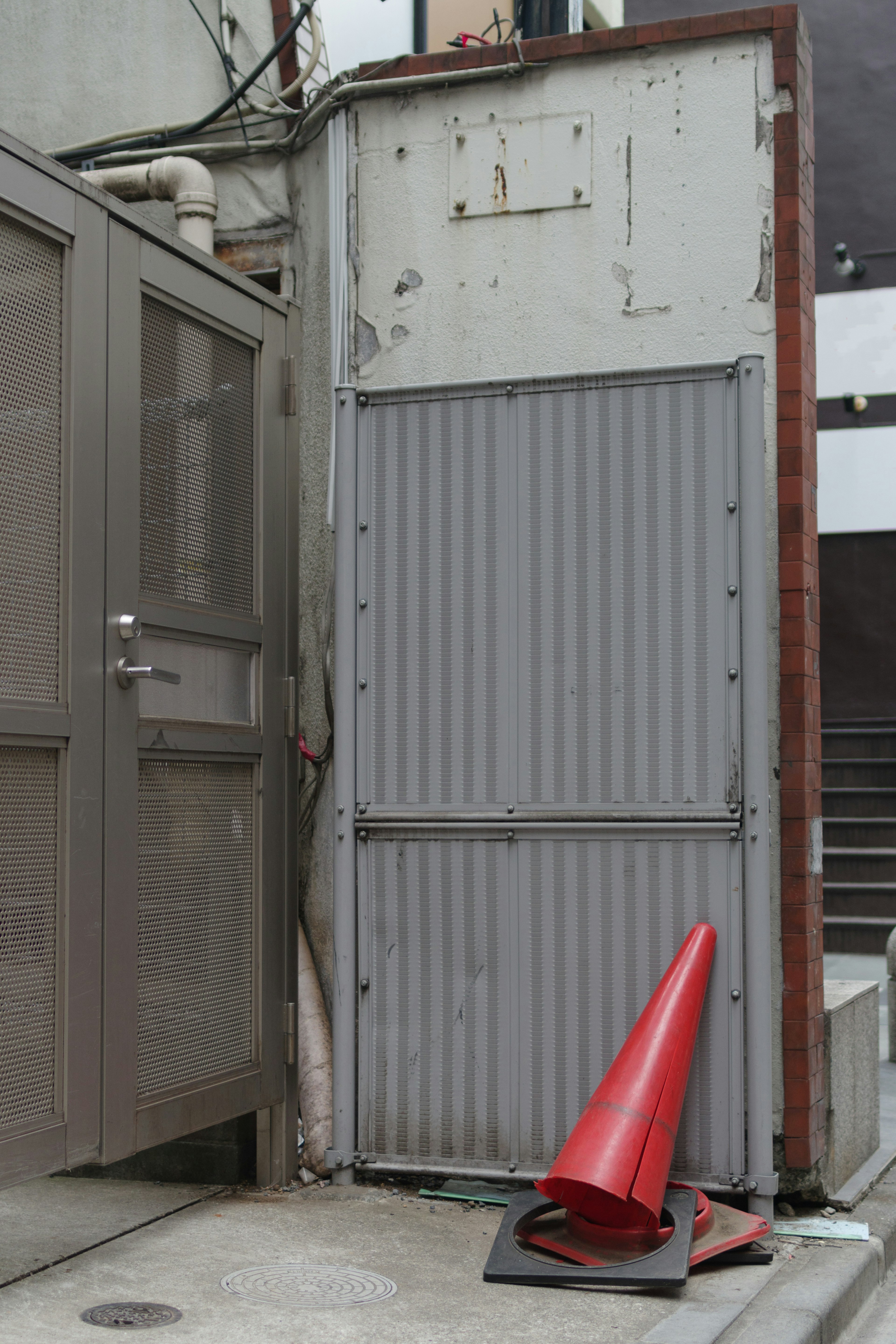 Narrow passageway featuring a gray metal door and a red traffic cone