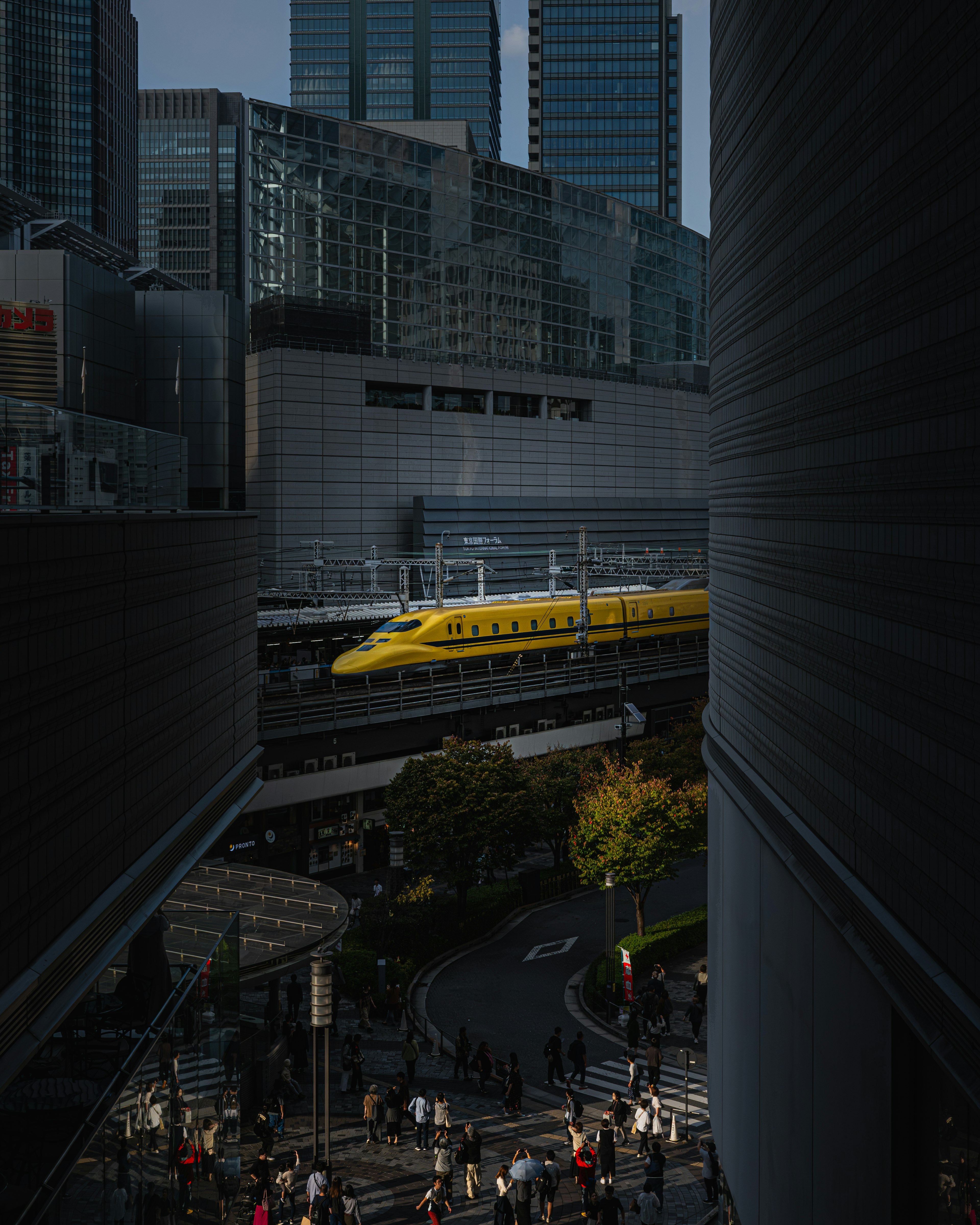 Yellow Shinkansen train in a bustling urban center with skyscrapers