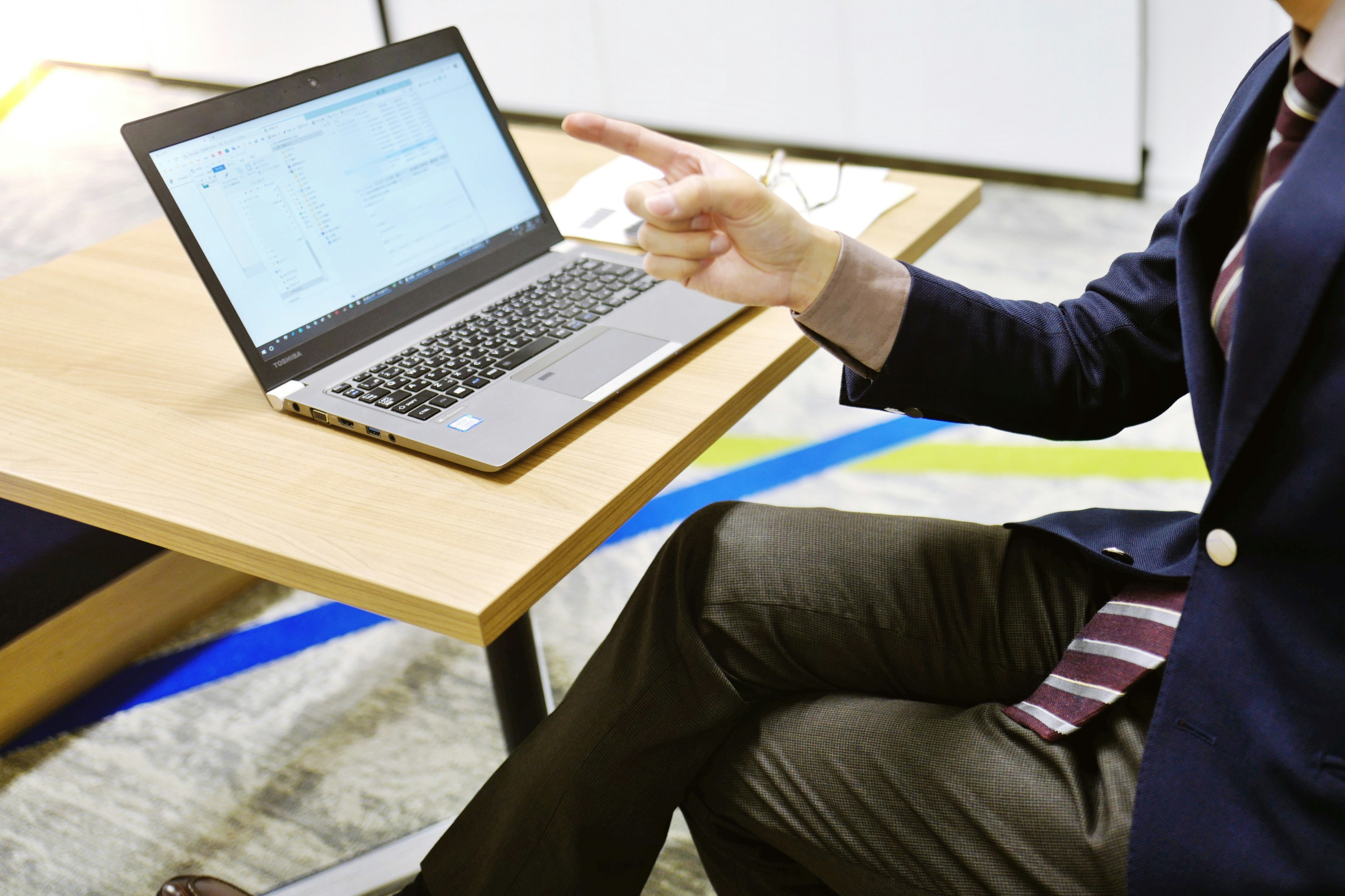 A man in a business suit pointing at a laptop on a wooden table