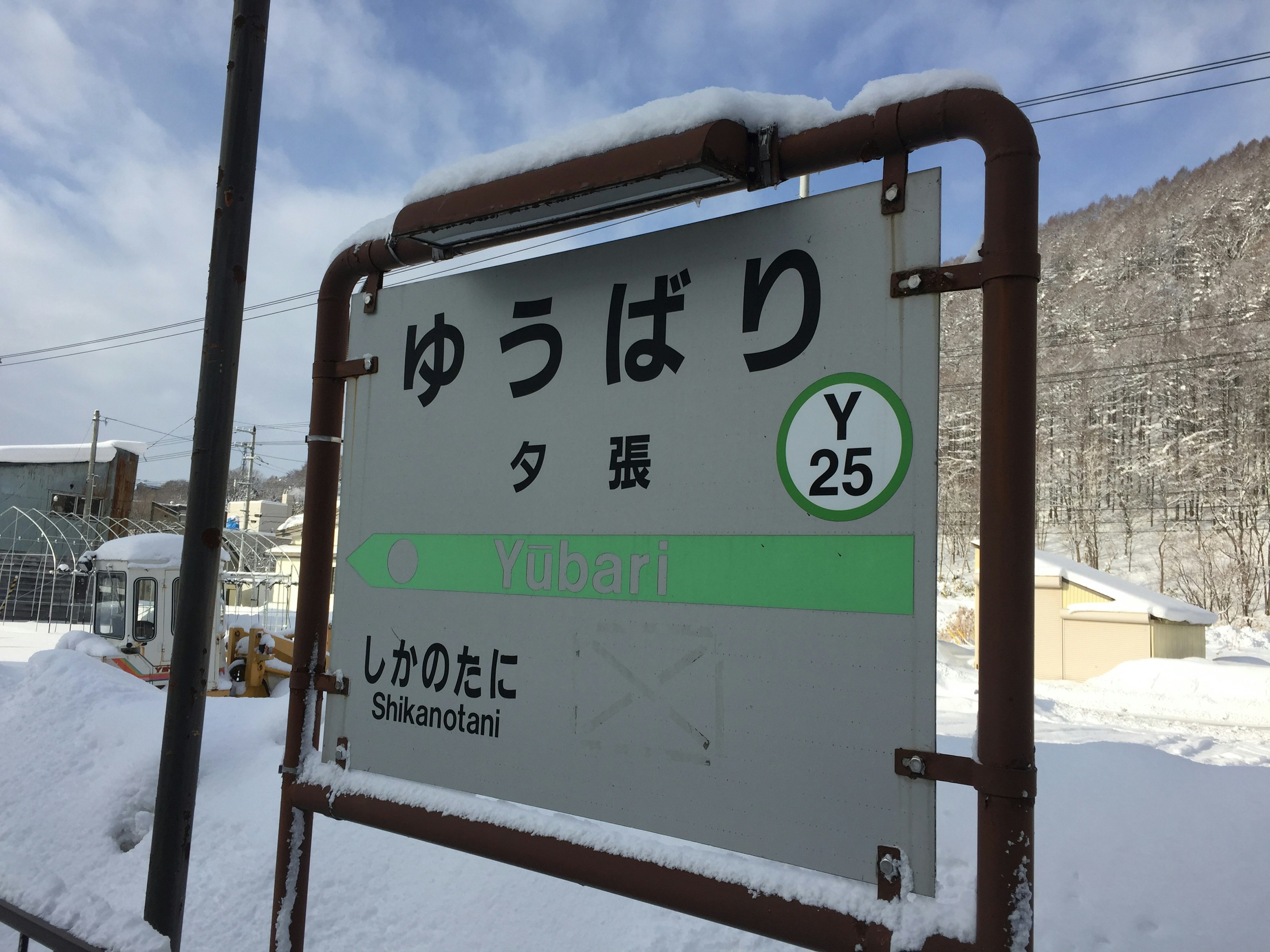 Schild der Yubari-Station, bedeckt mit Schnee, mit umliegender Landschaft