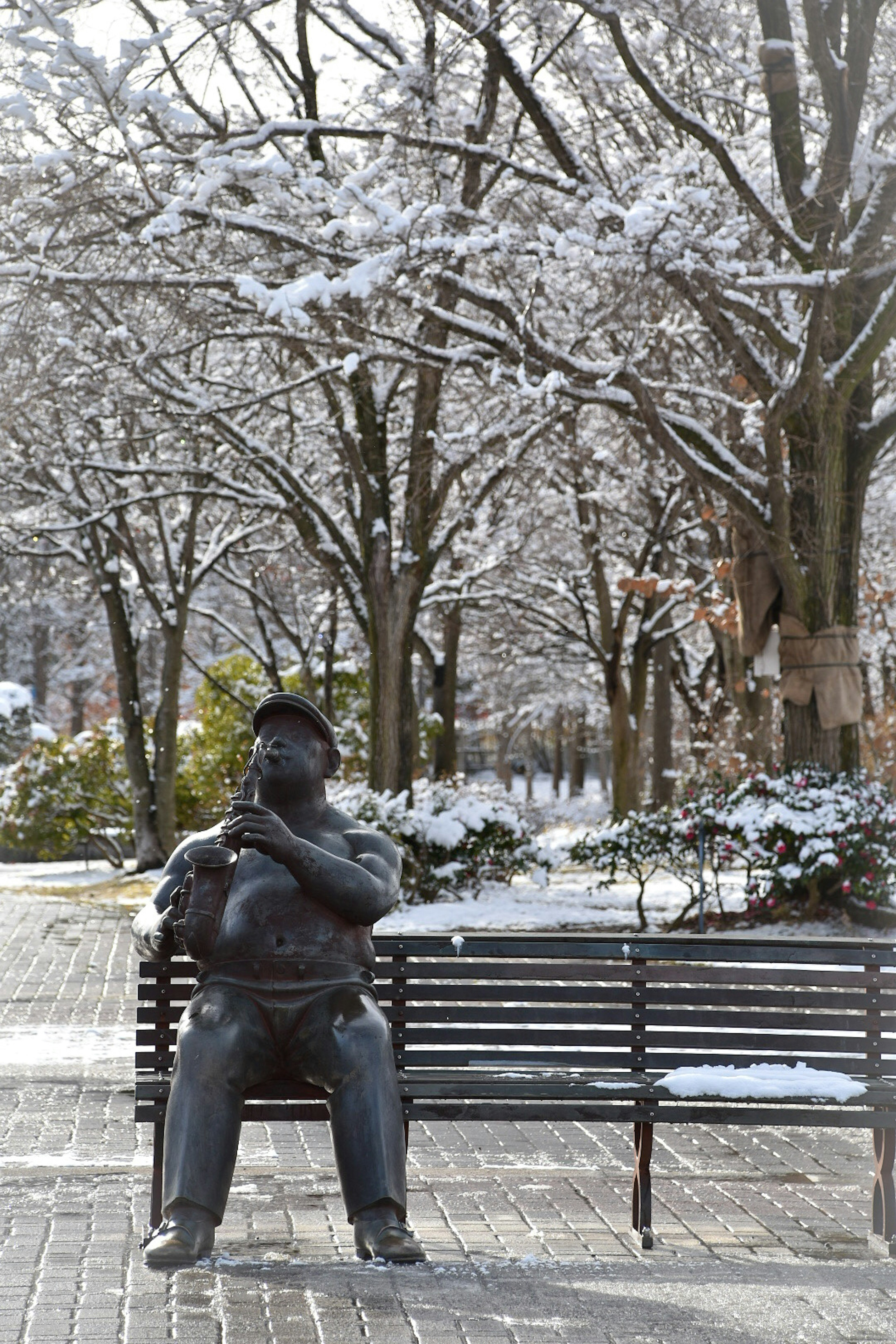 雪に覆われた公園でベンチに座る彫刻の男性