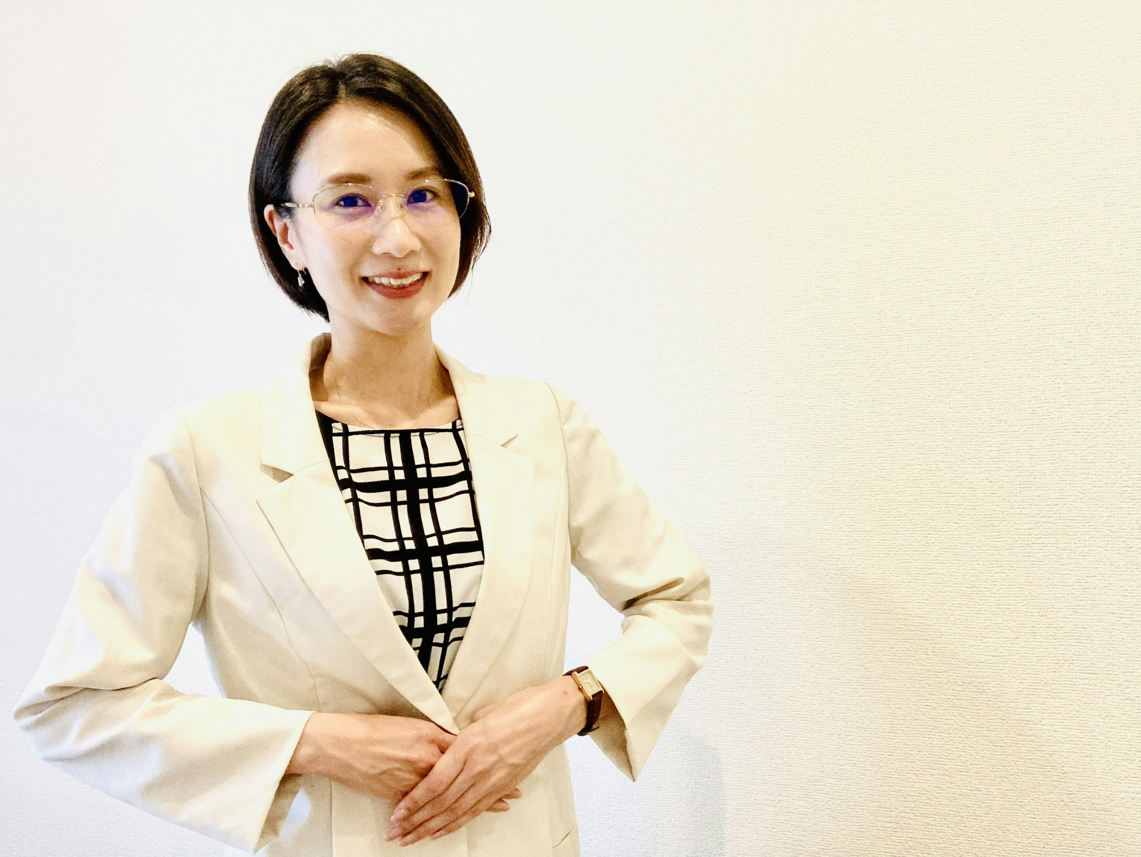 Une femme souriante devant un fond blanc portant un costume d'affaires et des lunettes