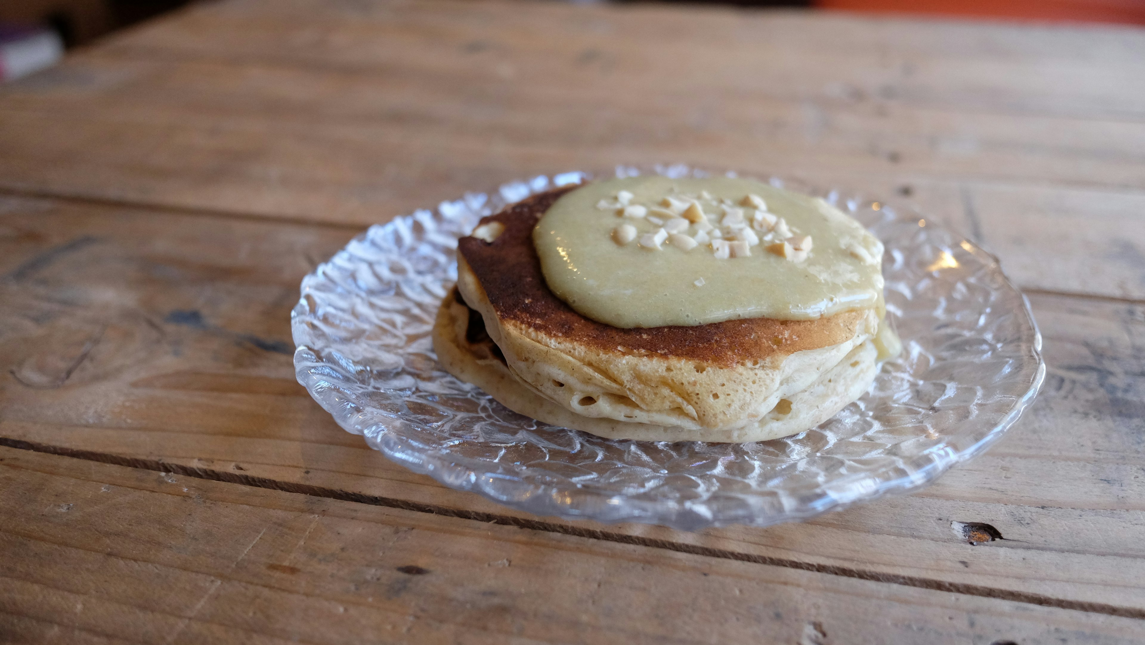 Pancake topped with green cream and pine nuts on a glass plate