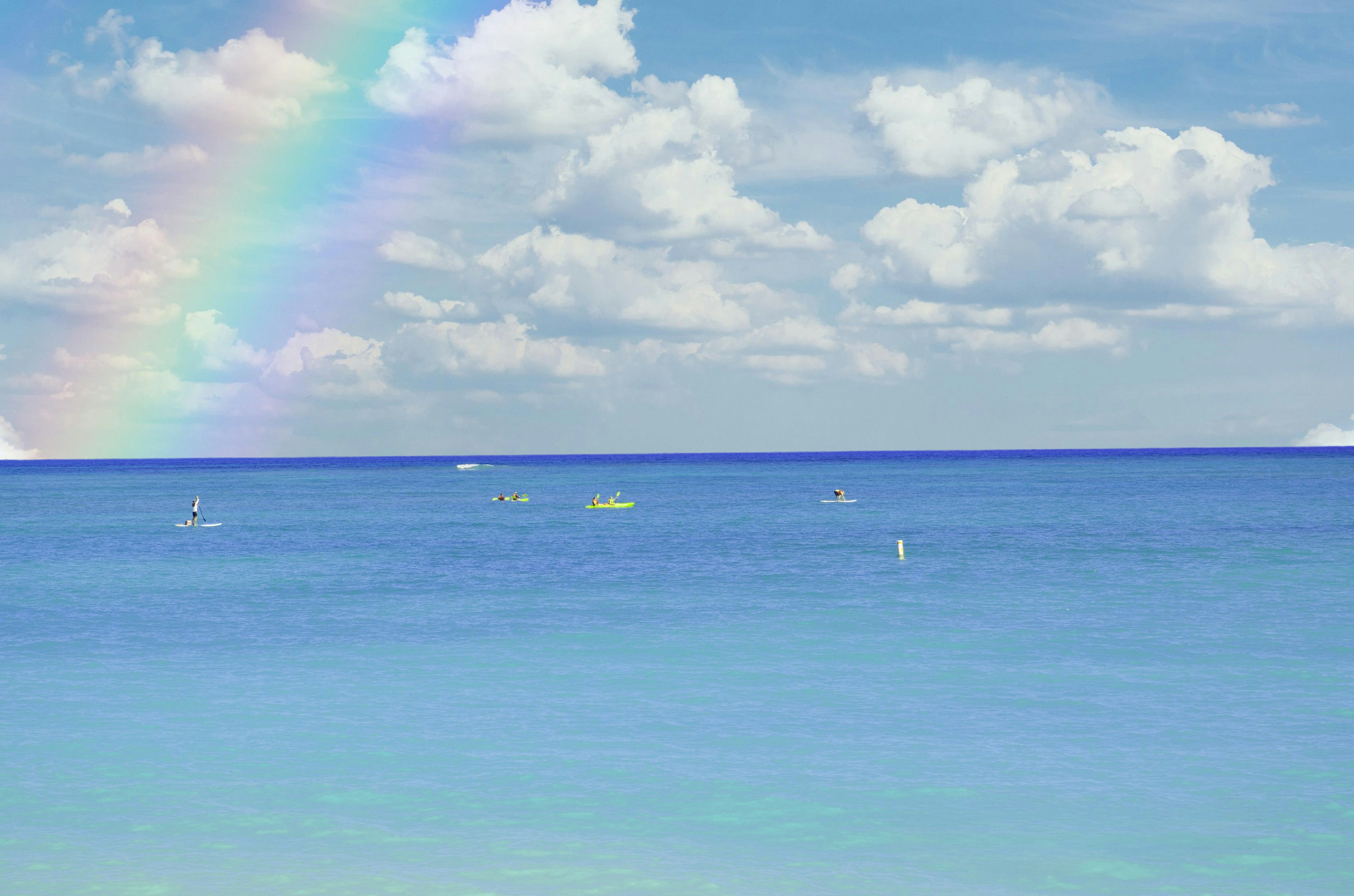 Scenic view of the ocean with a rainbow and kayakers