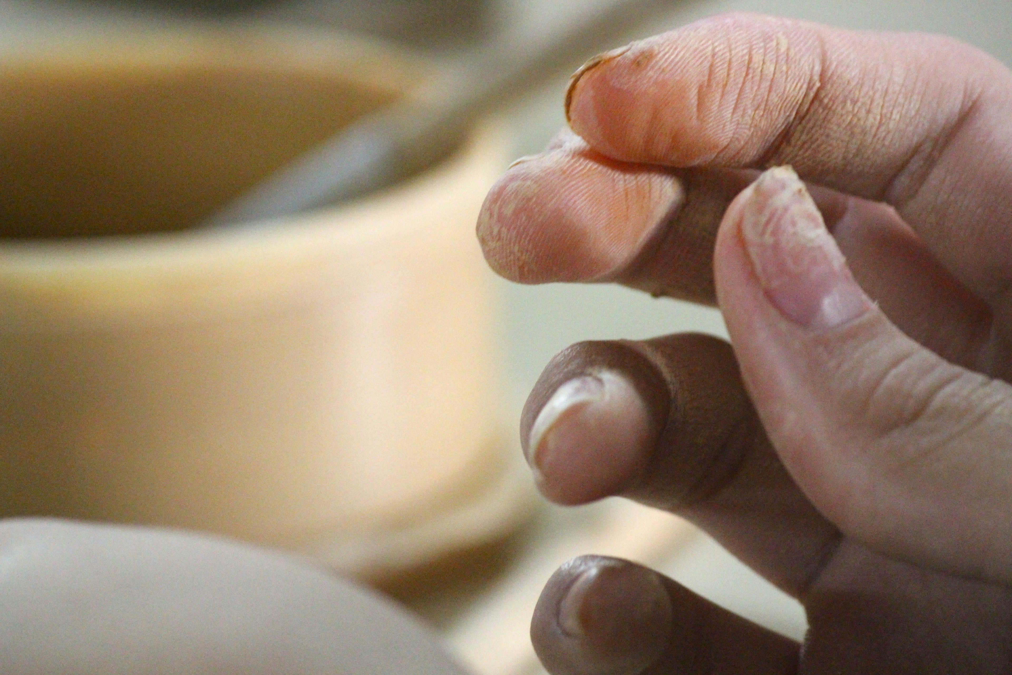 A hand with clay-covered fingers shaping pottery