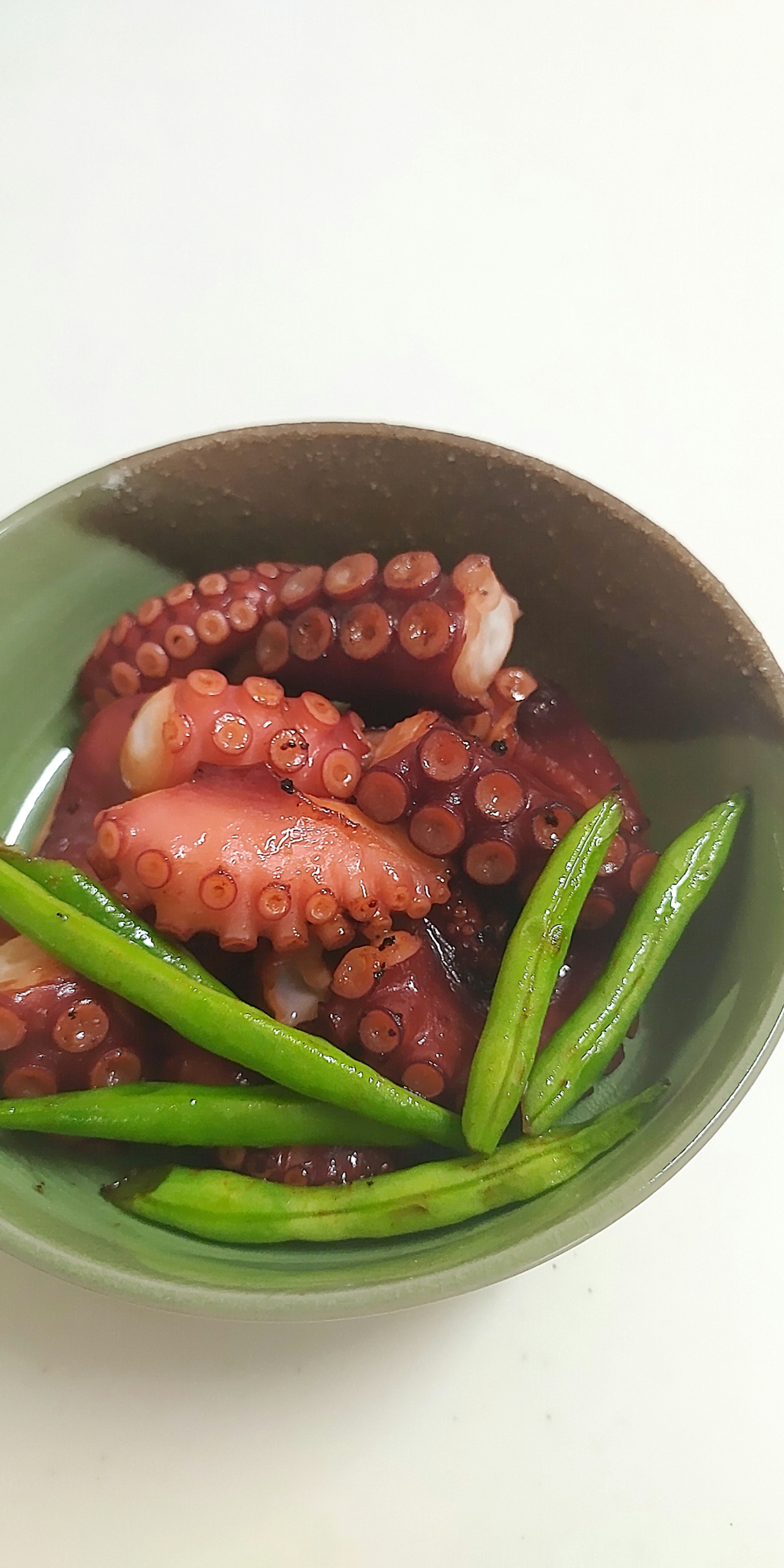 A bowl of cooked octopus served with green vegetables