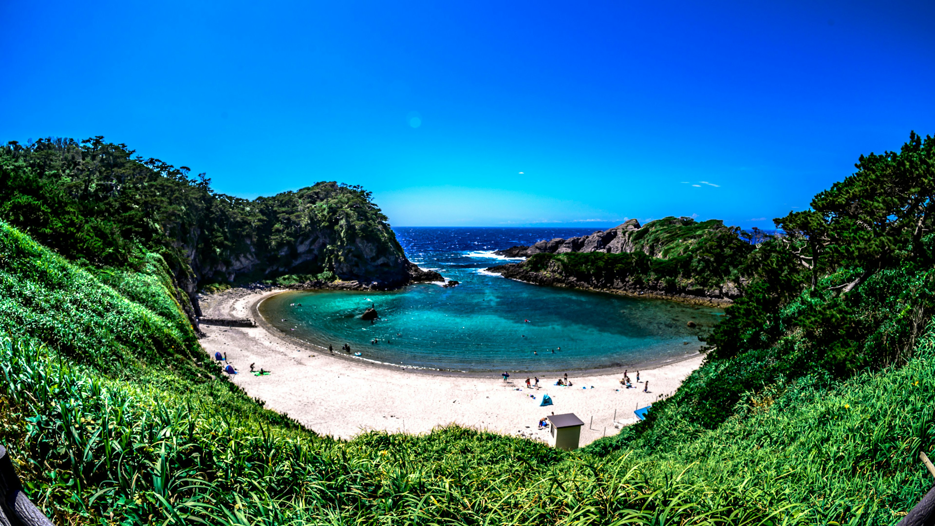 Scenic view of a beach surrounded by green hills and clear blue water