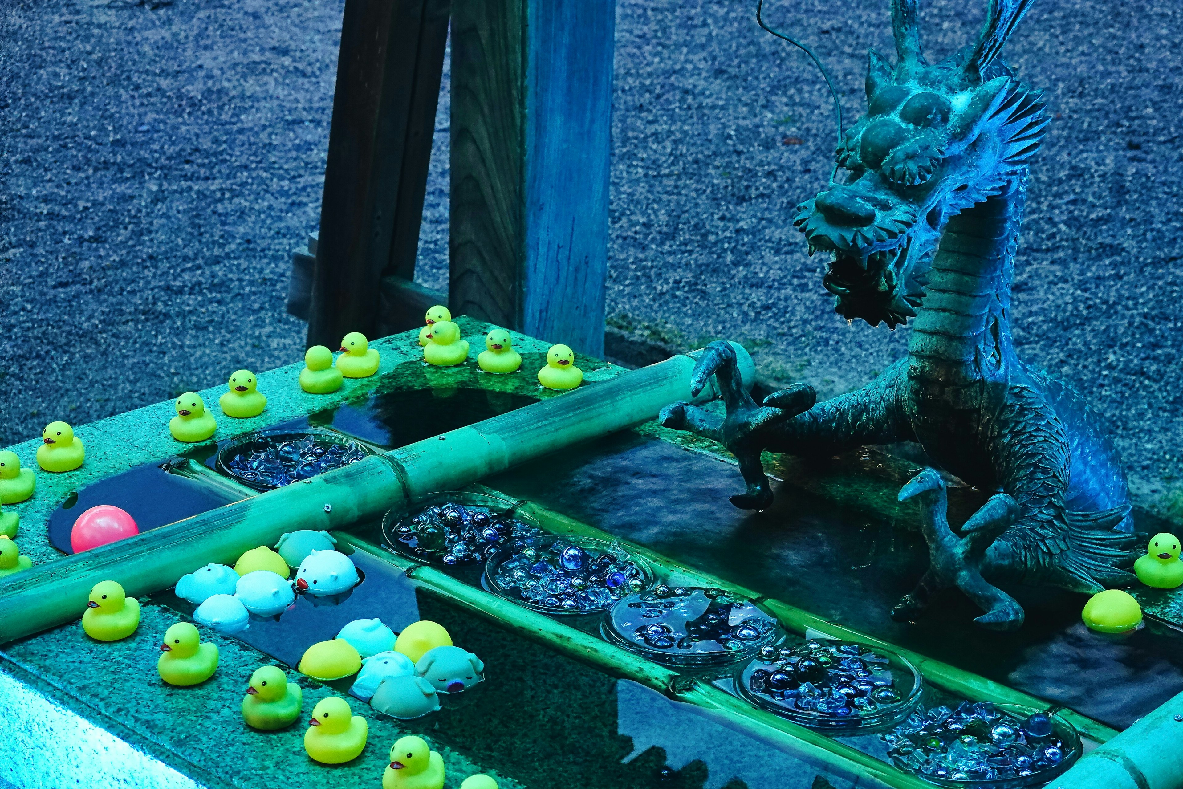 Statue de dragon sous une lumière bleue avec des canards en caoutchouc jaunes et du bambou