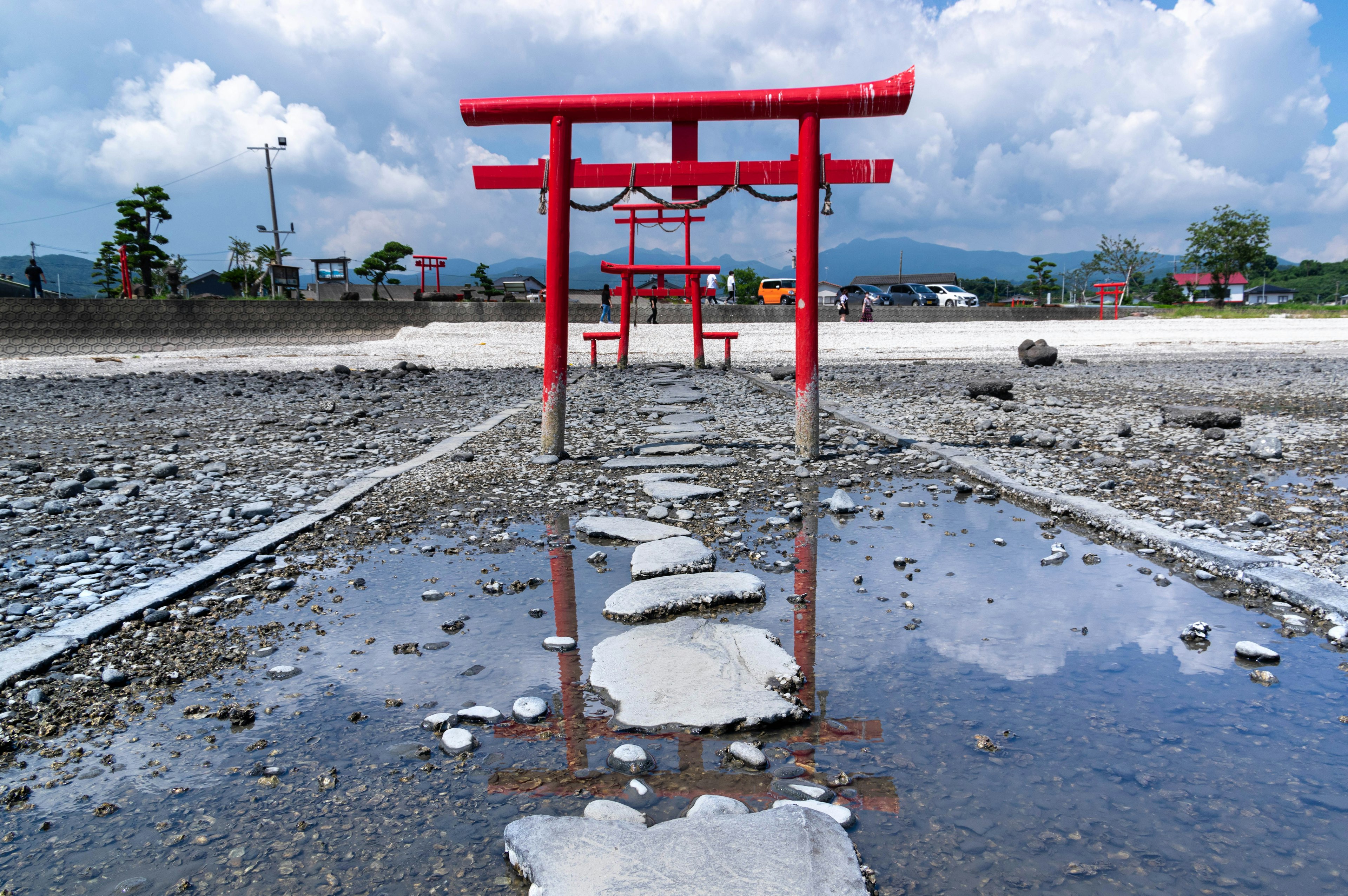 A red torii gate reflected in a puddle with a rocky path