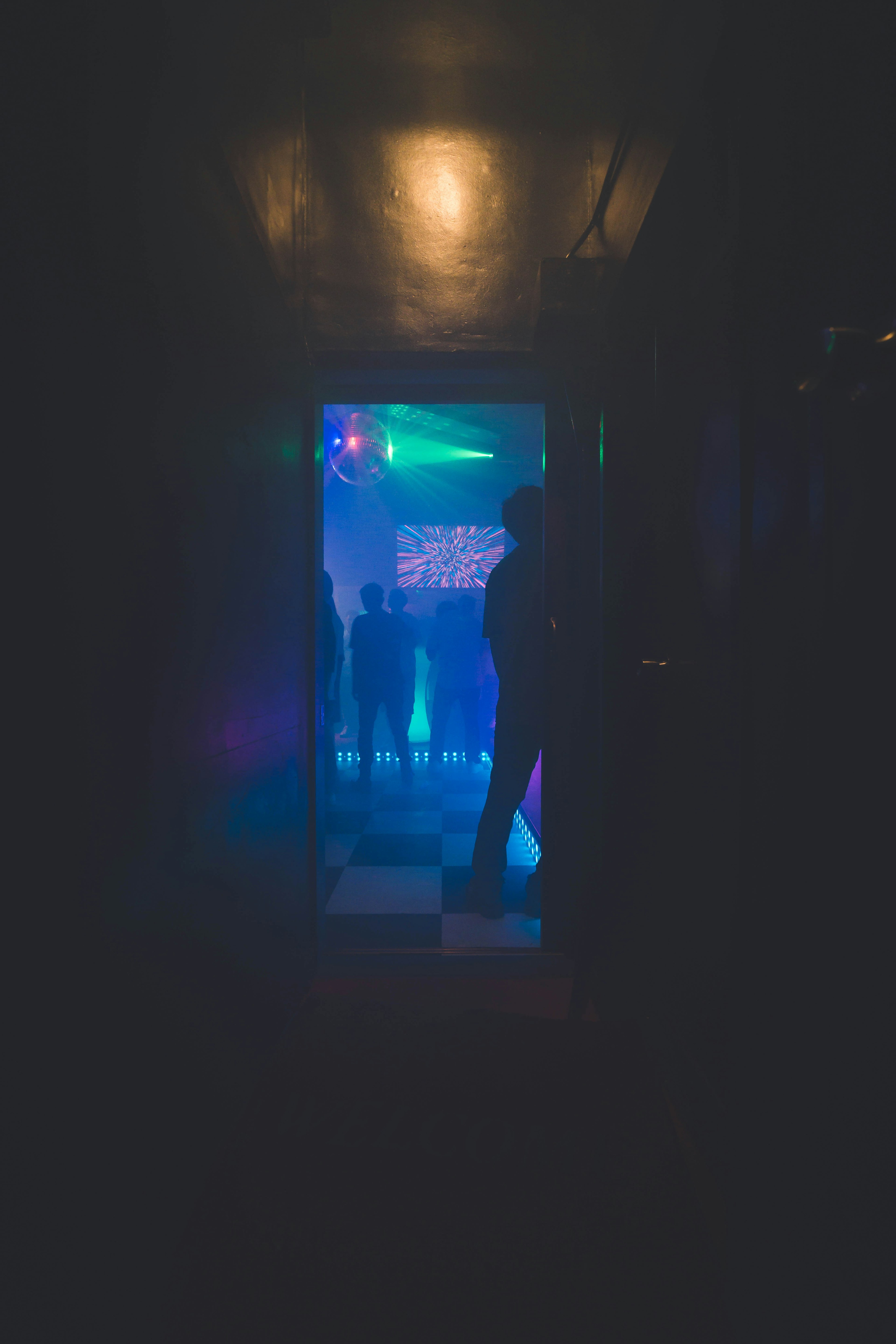 Dimly lit hallway leading to a vibrant club scene with blue and green lights