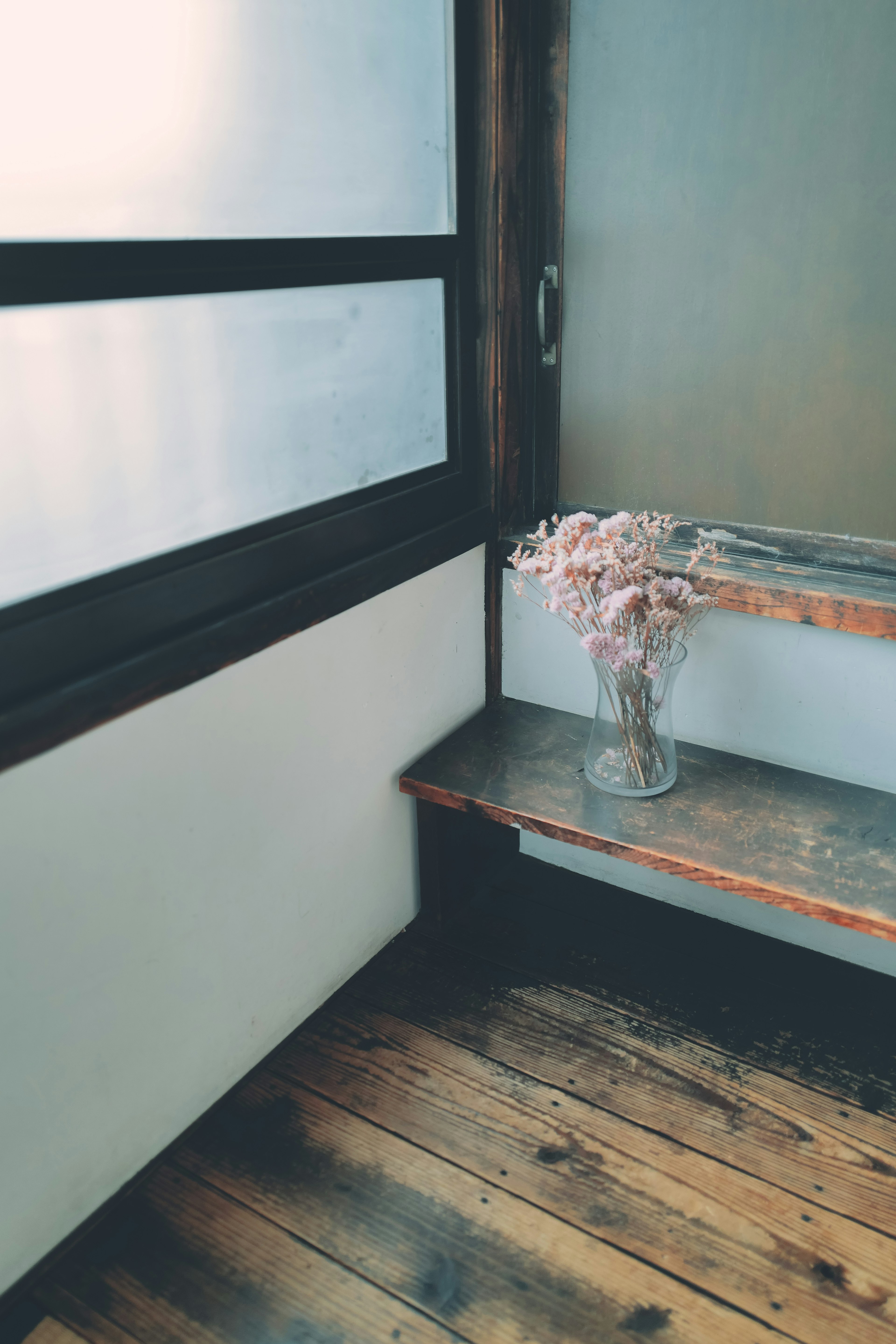 Bright corner of a room featuring a vase with flowers and a wooden bench