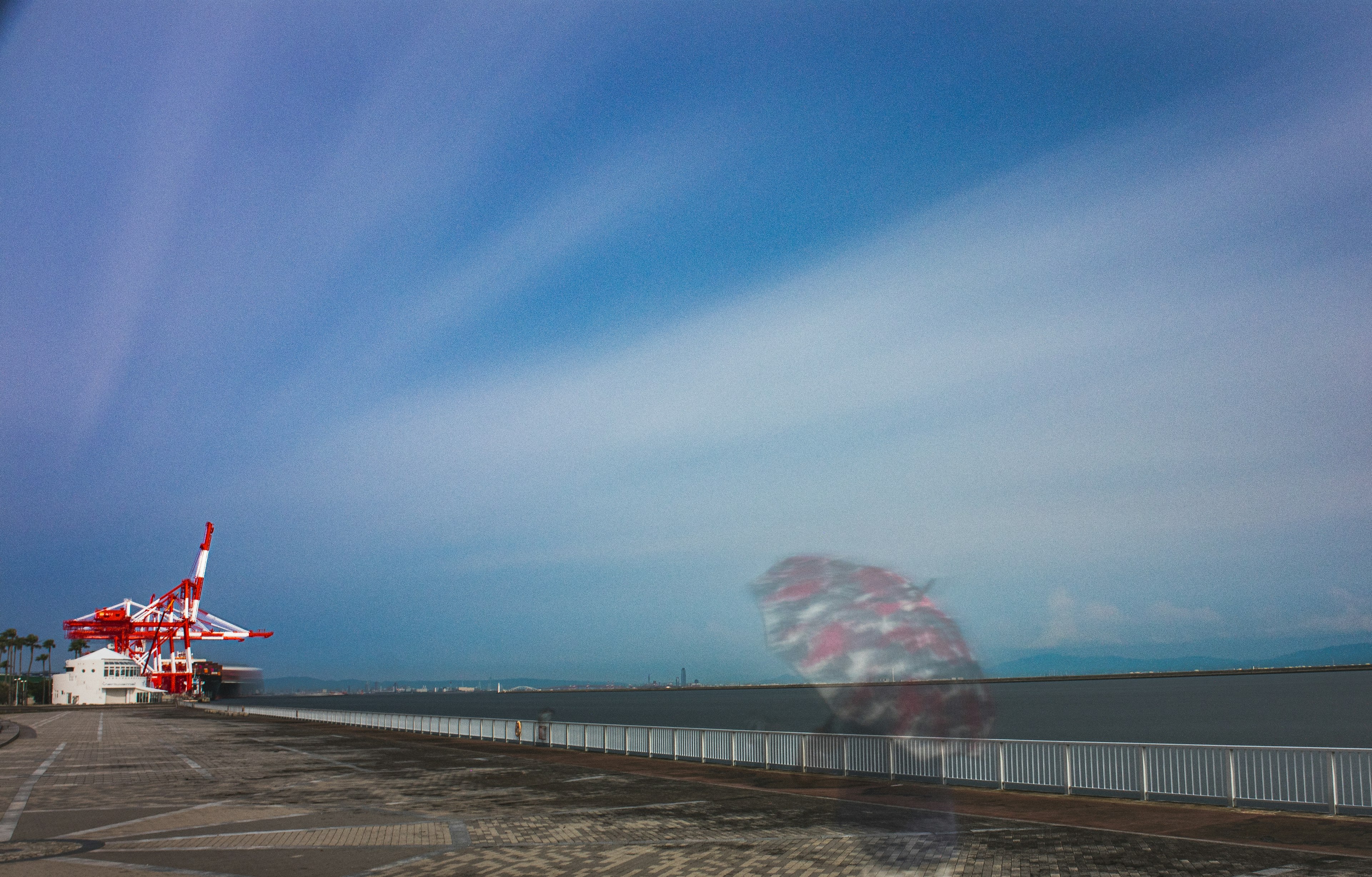 青空と雲のストライプが広がる海岸の風景に赤い船が見える