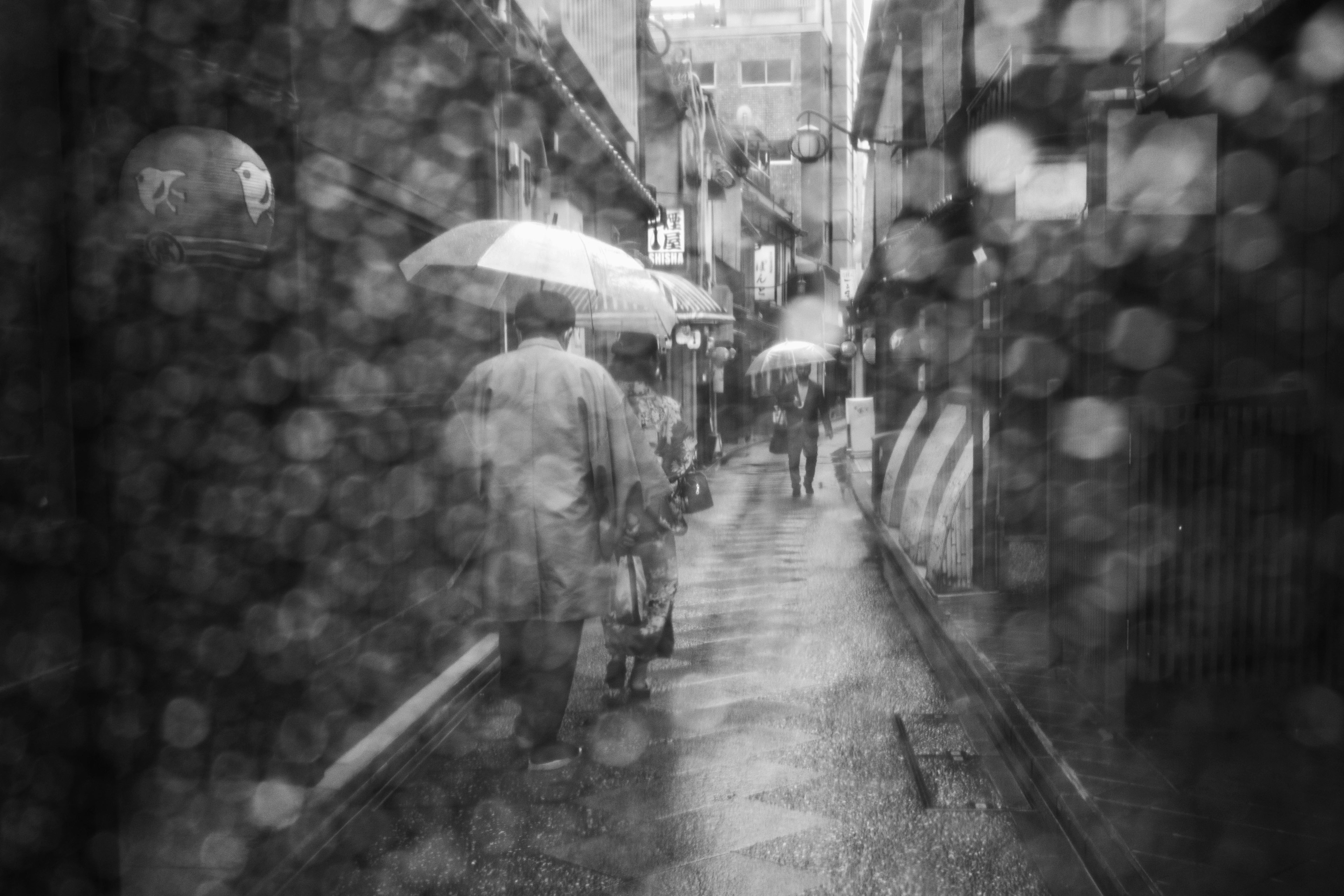 在狹窄巷道中走在雨中的人們，手持雨傘