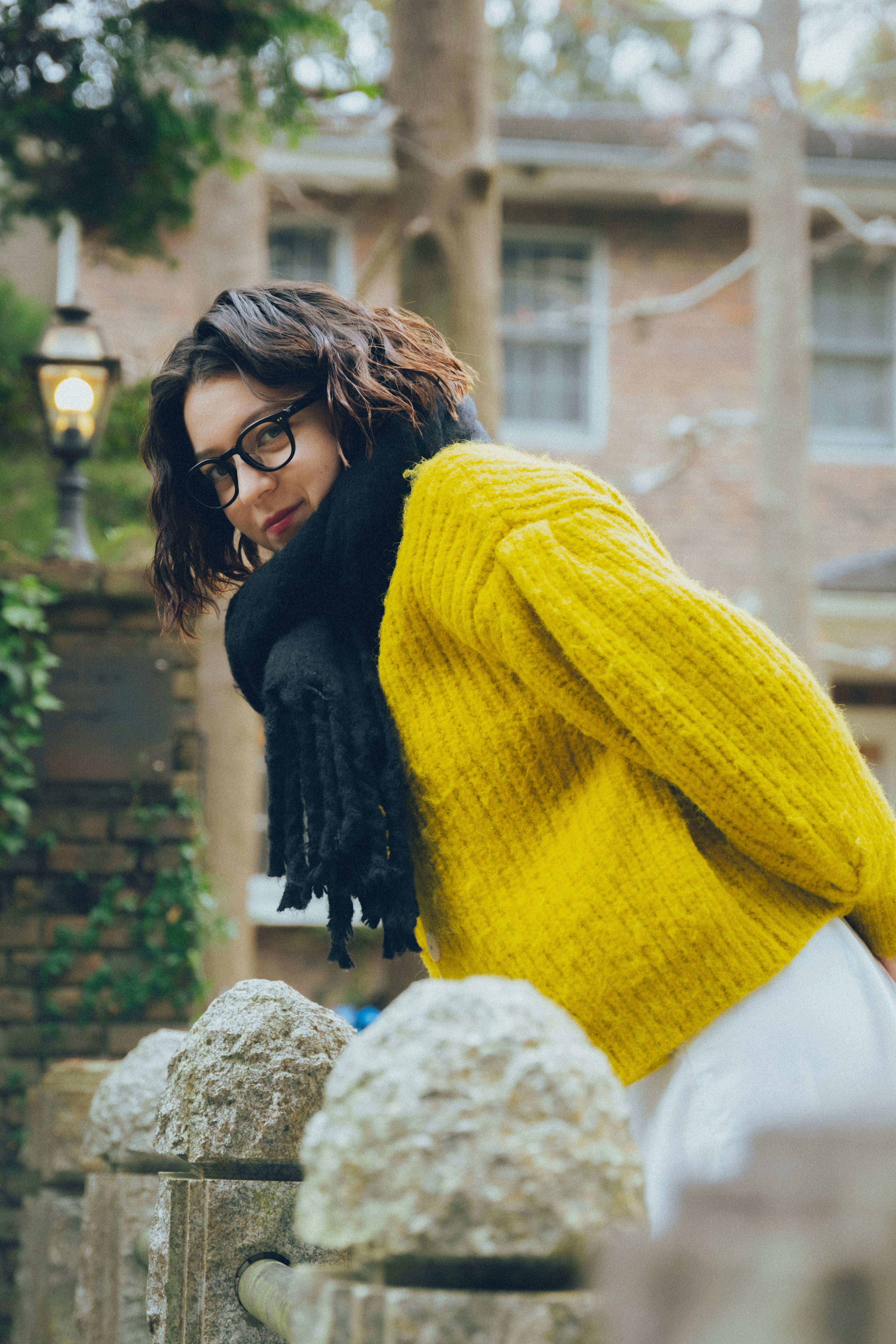 Woman in a yellow sweater leaning over a stone fence smiling