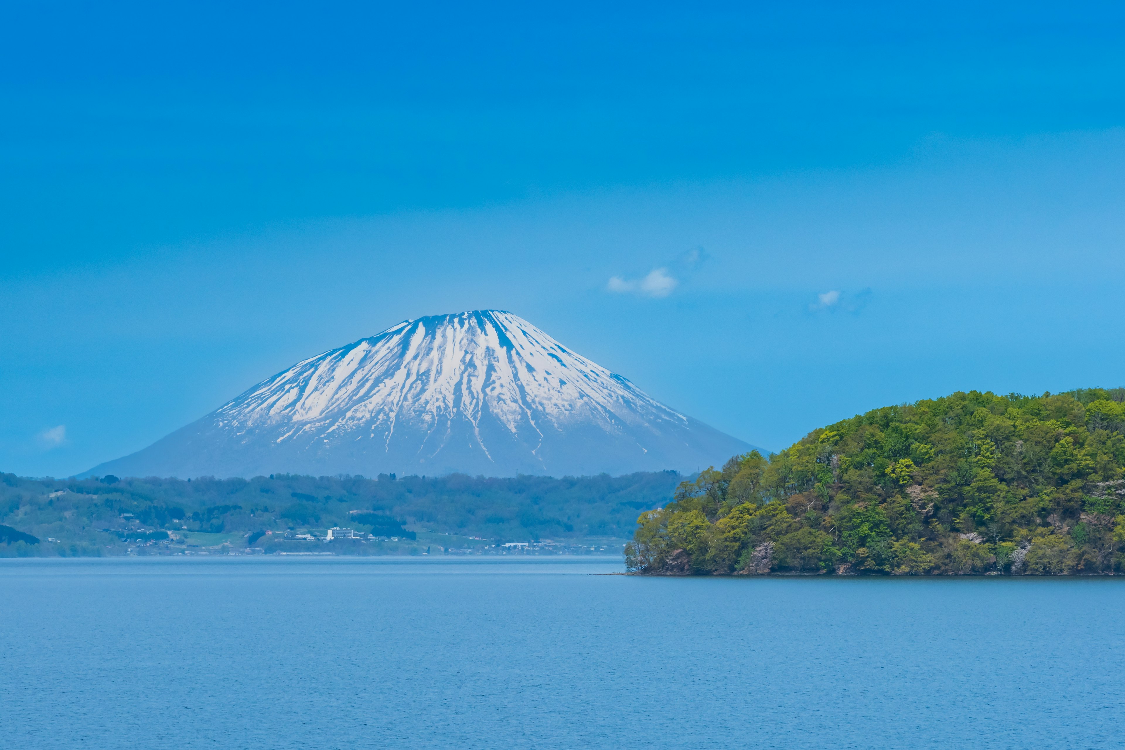 美しい青空の下に雪をかぶった山と緑の島が見える風景