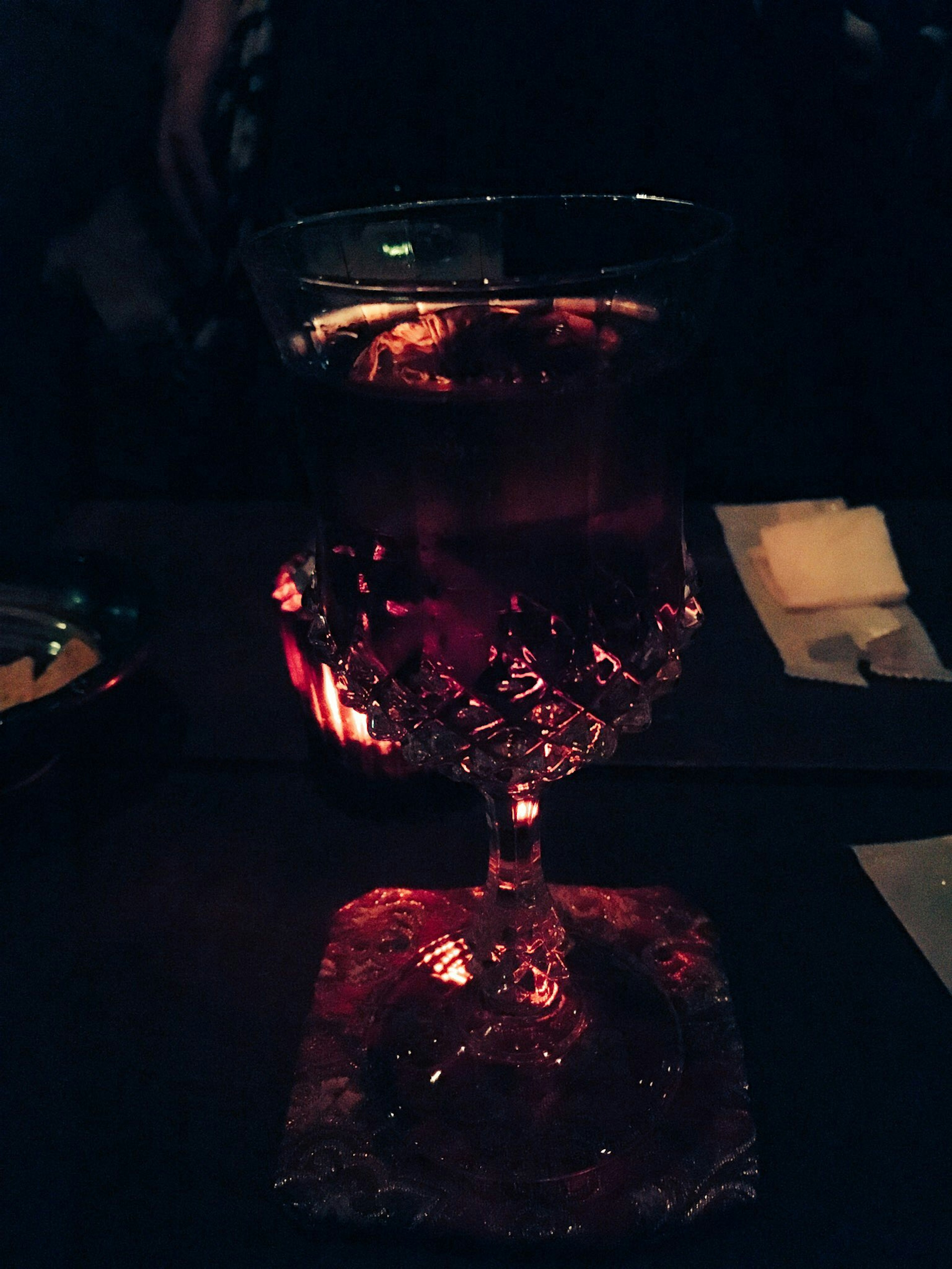 A crystal glass filled with a red beverage against a dark background