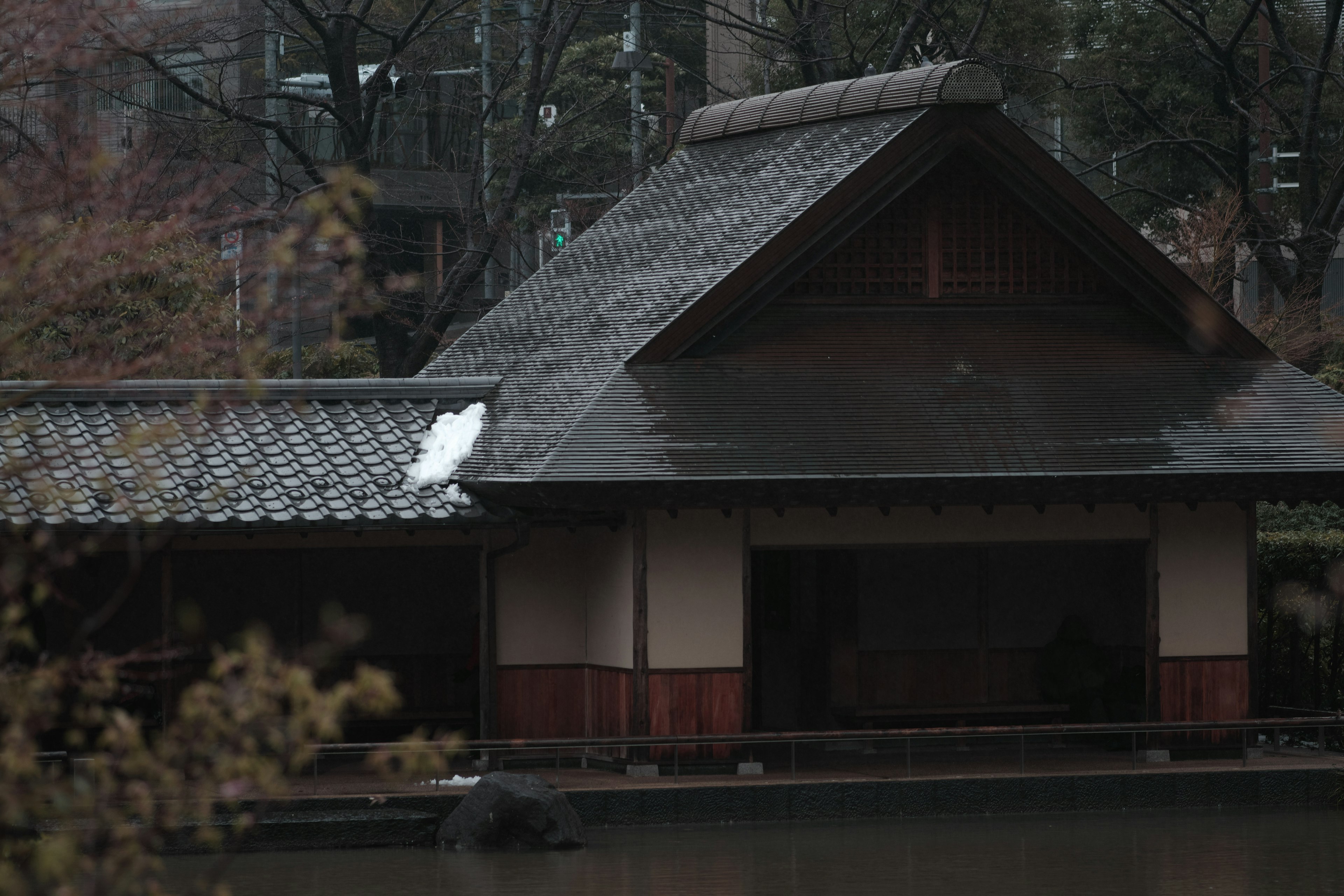 Rumah tradisional Jepang di tepi kolam tenang dengan hujan jatuh di atap