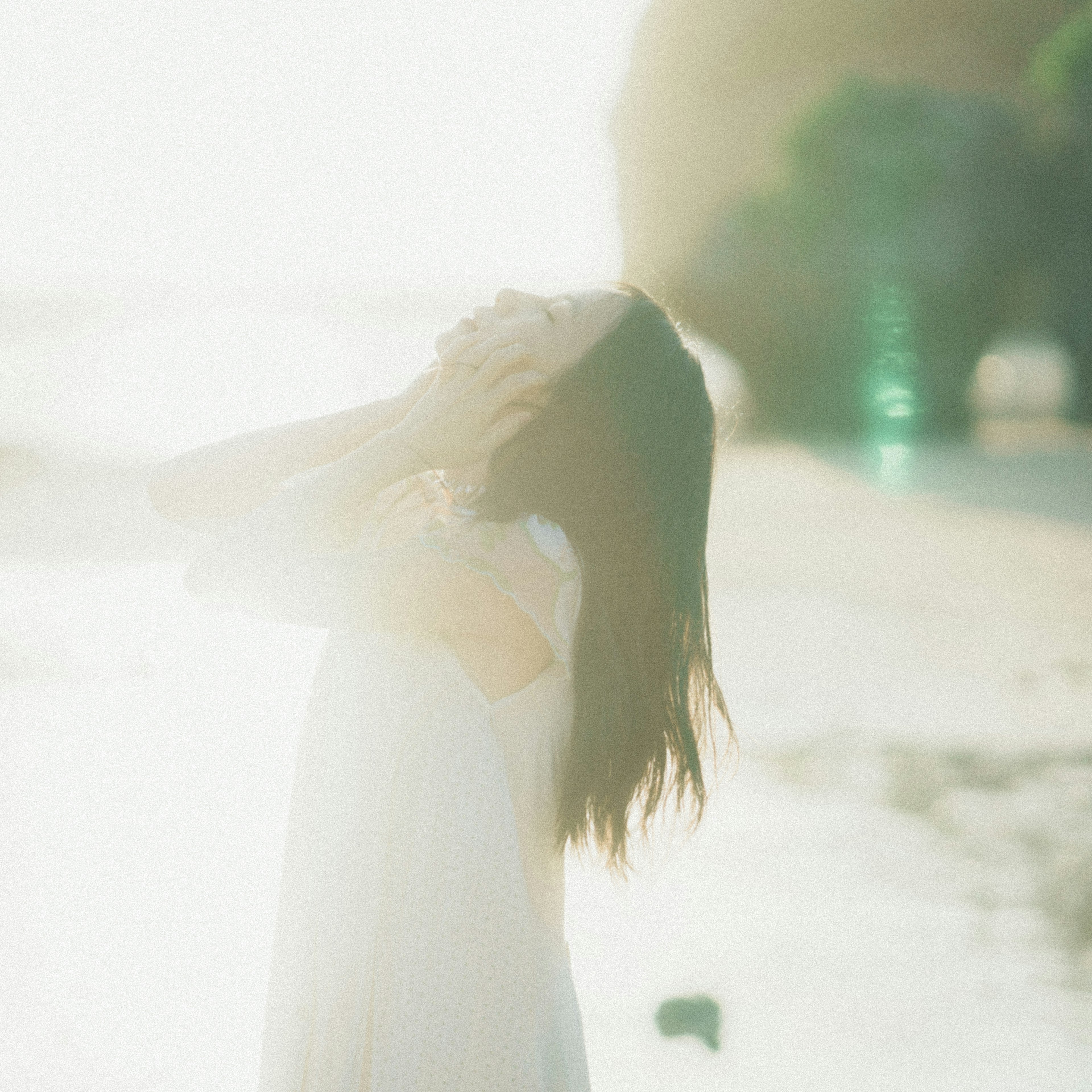 Silhouette di una donna in abito bianco che si copre il viso sulla spiaggia