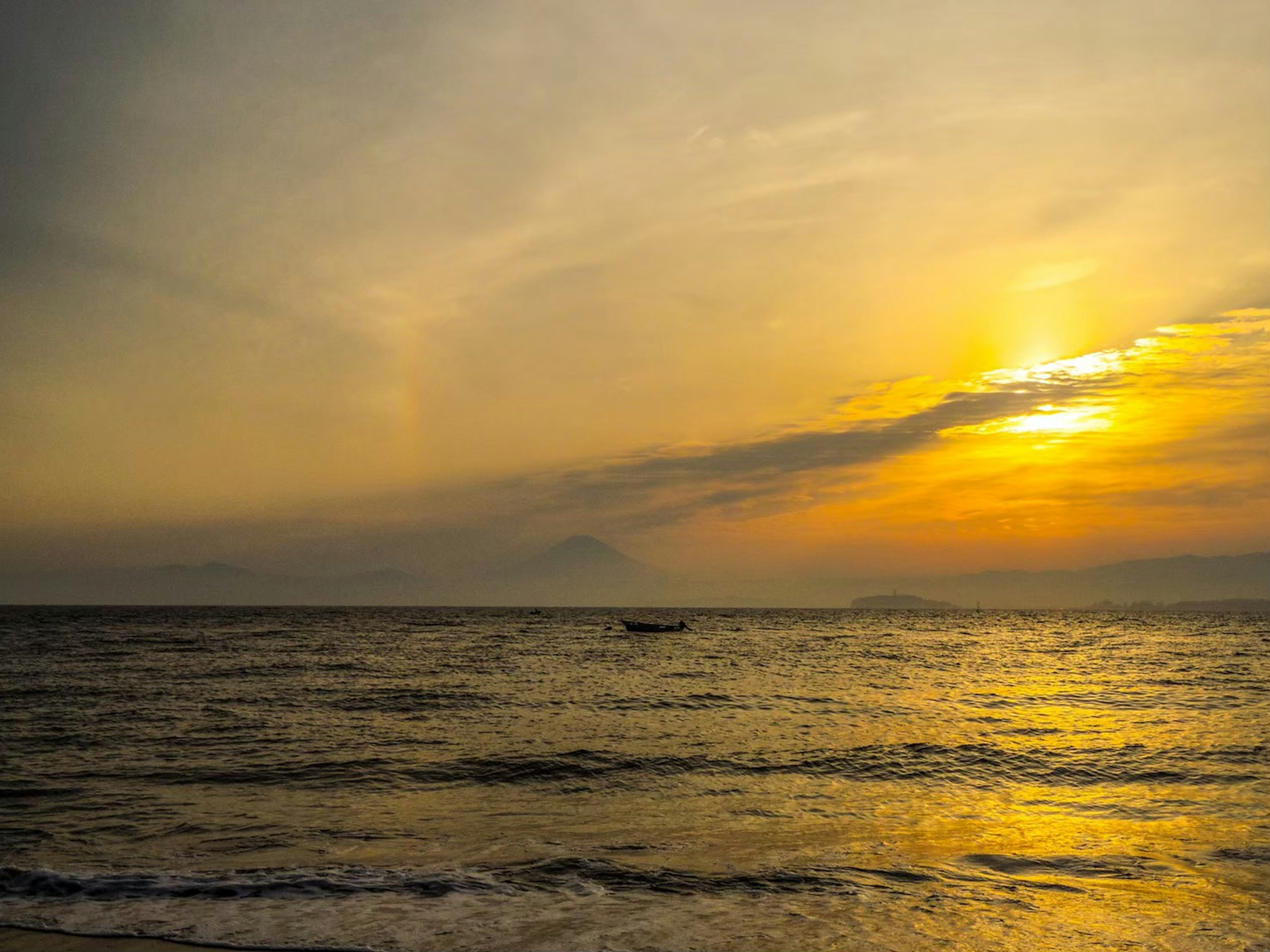 Matahari terbenam di lautan dengan perahu di kejauhan