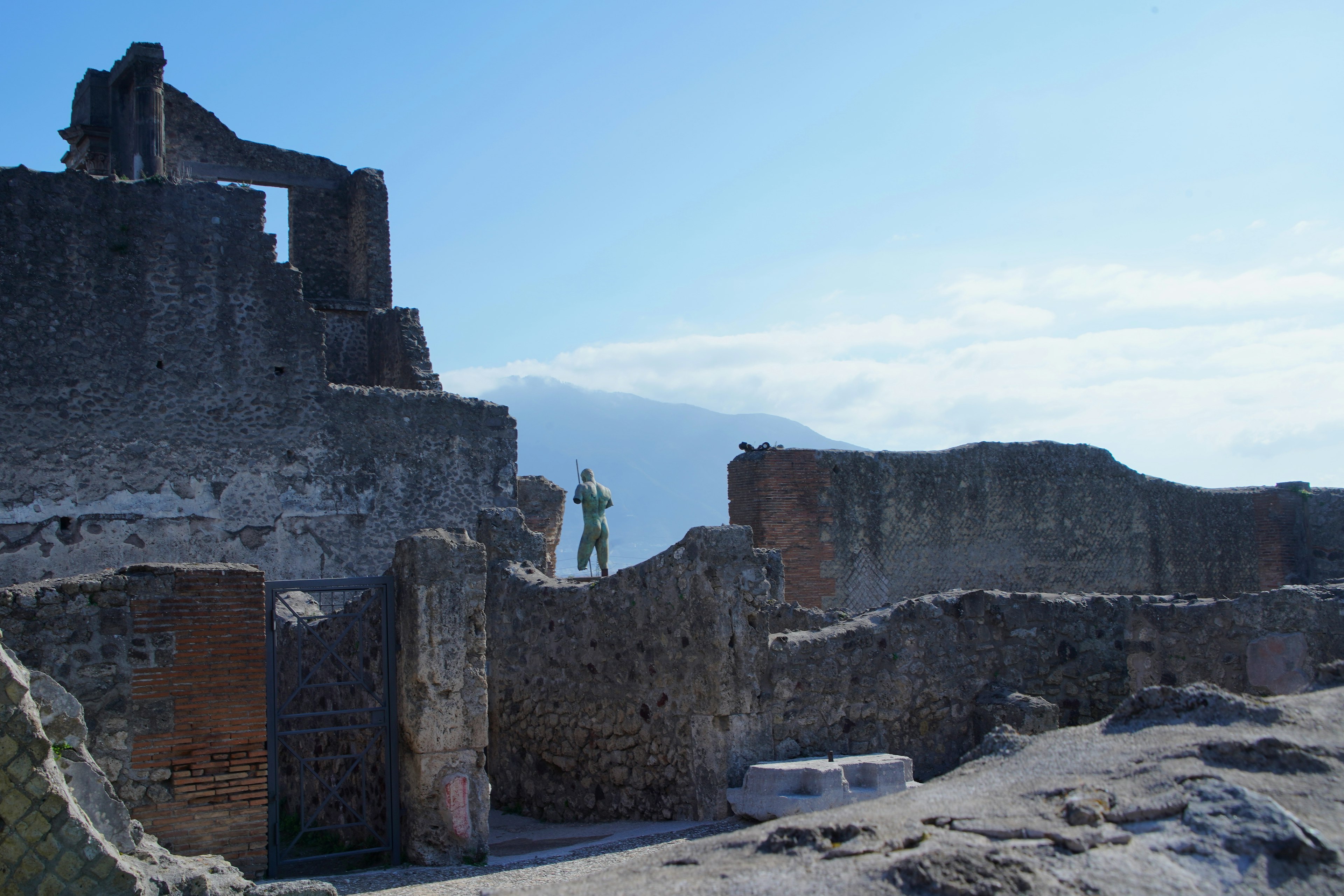 Un turista in piedi tra le rovine di Pompei con strutture antiche e un cielo blu chiaro