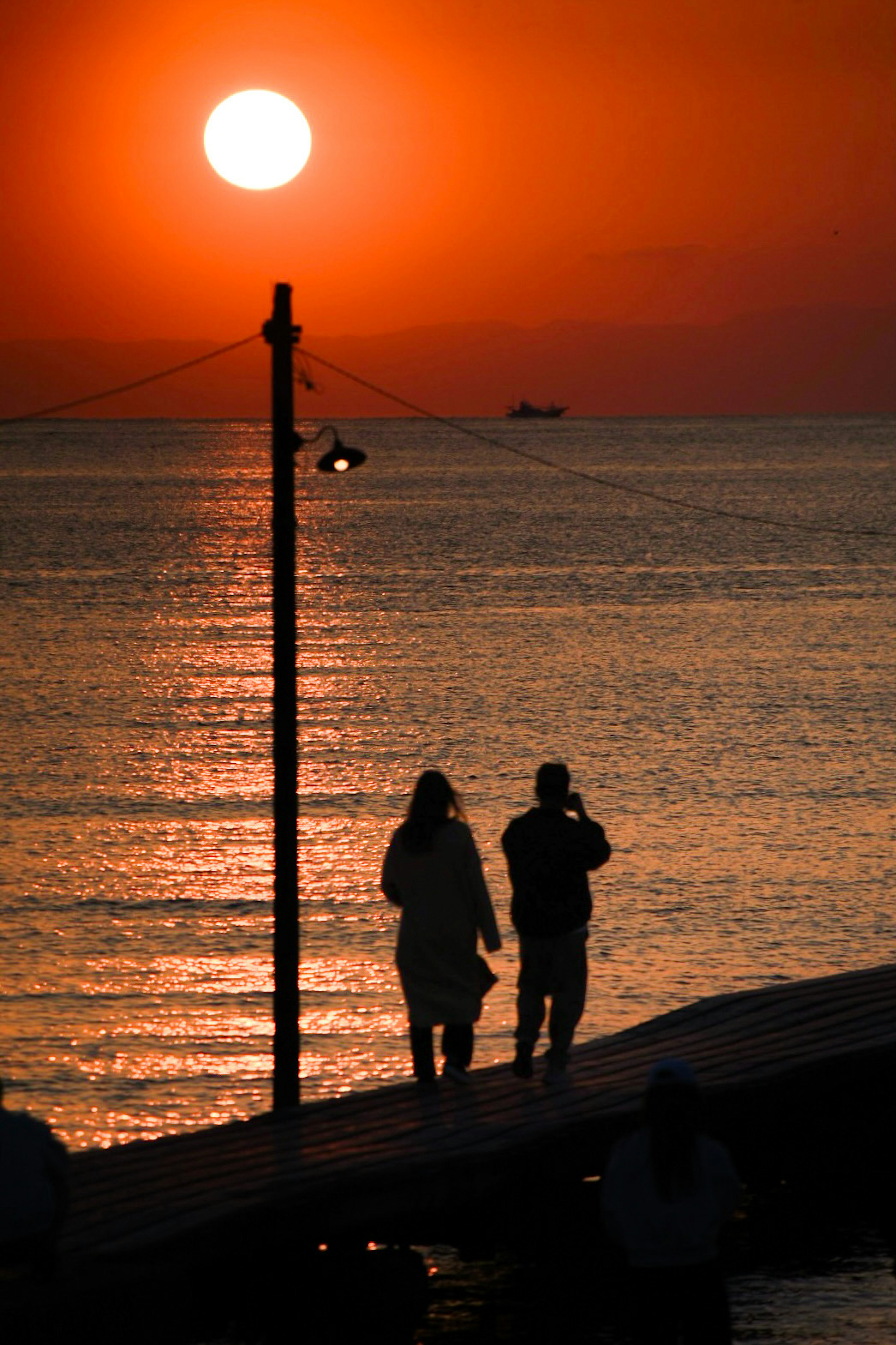 Silueta de dos personas caminando en un muelle con un atardecer de fondo