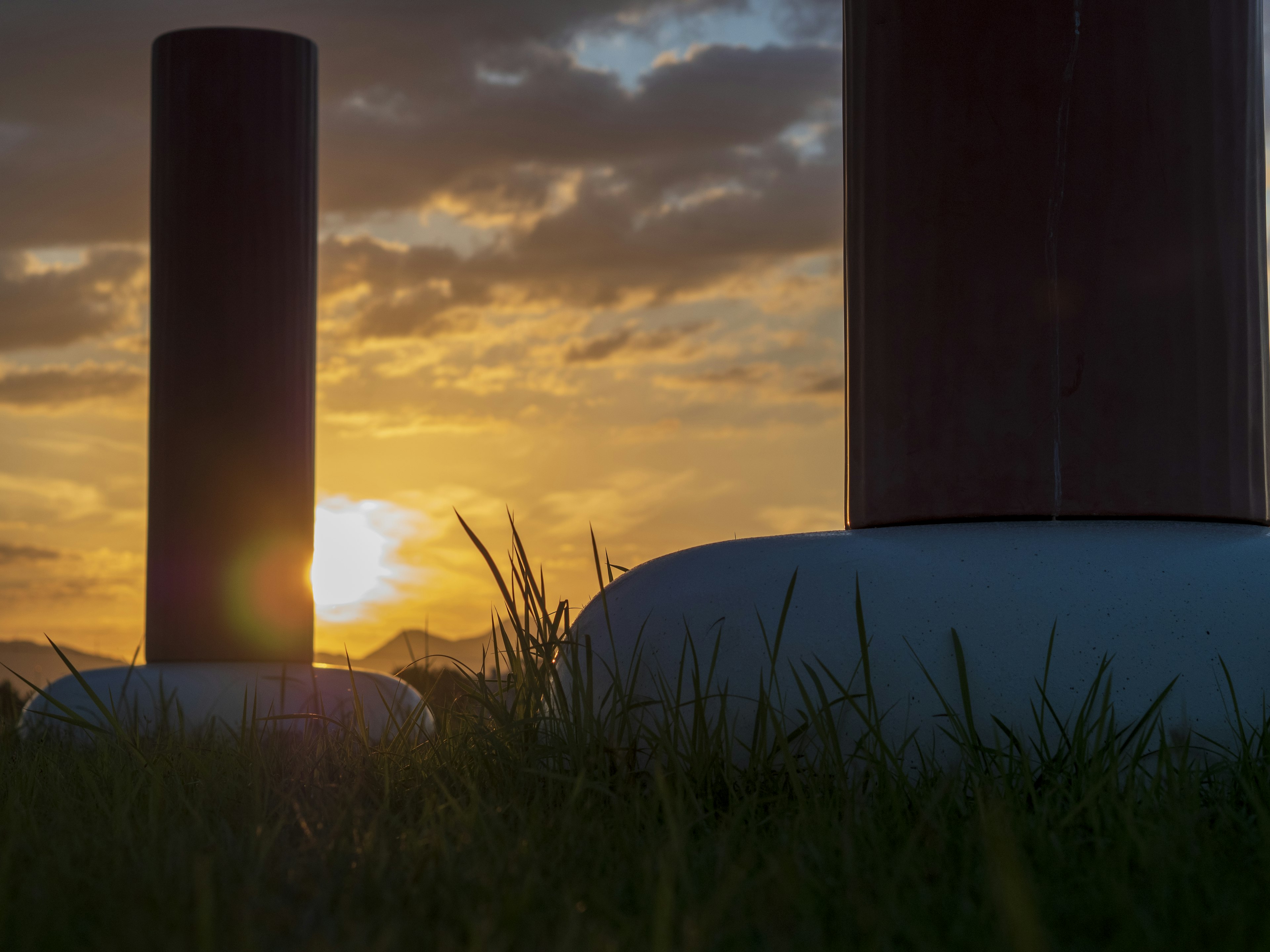 Two pillars silhouetted against a sunset with grass in the foreground